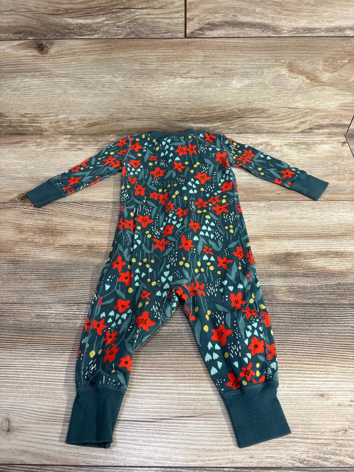 Green long sleeve baby romper with red floral print on wood background