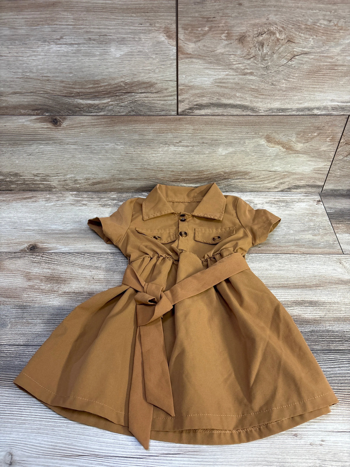 Flat lay of brown belted polo dress, size 3-4T, showing short sleeves, chest pockets and tied waist belt on wood floor