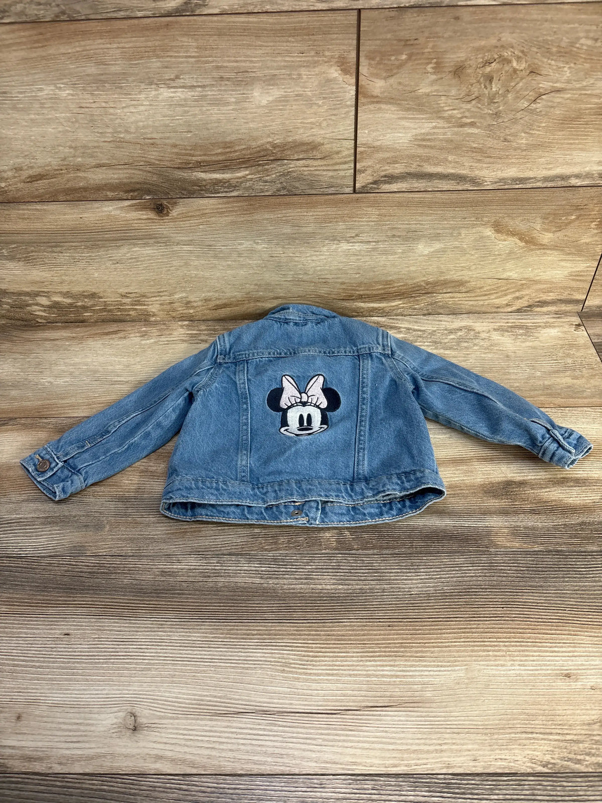 Back view of Baby Gap x Disney Minnie Mouse denim jacket showcasing Minnie Mouse graphic applique with wood-grain background