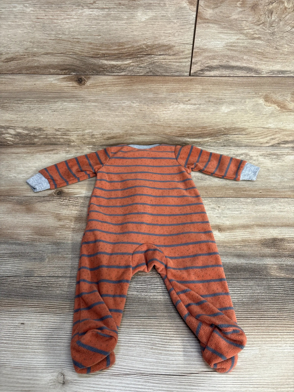 Orange and gray striped baby footed sleeper on wood floor background