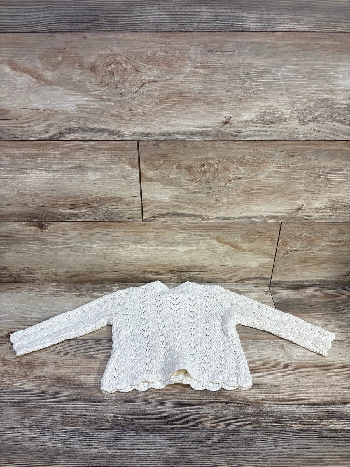 Flat lay of ivory embroidered knit cardigan showing eyelet knit pattern, scalloped hem and long sleeves on wood background