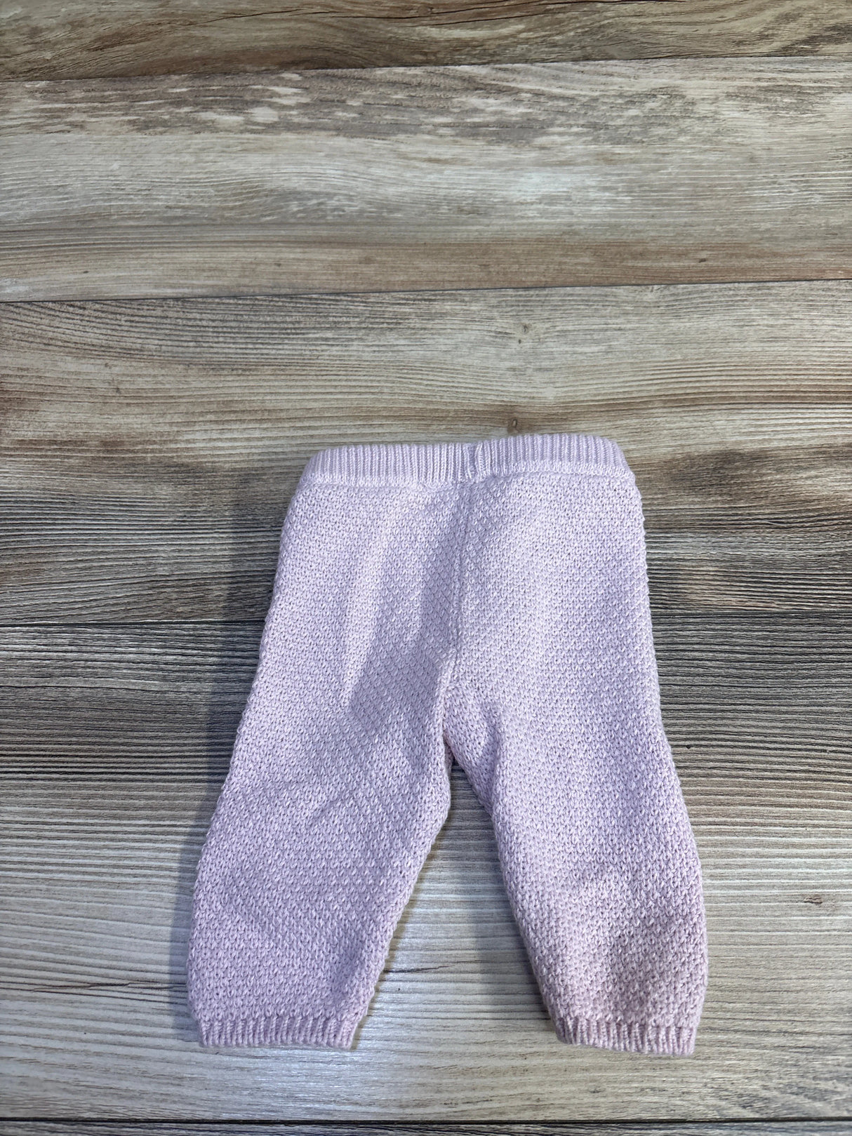 Flat lay of newborn pink knit baby pants showing textured knit, ribbed waistband and cuffs on light wood background