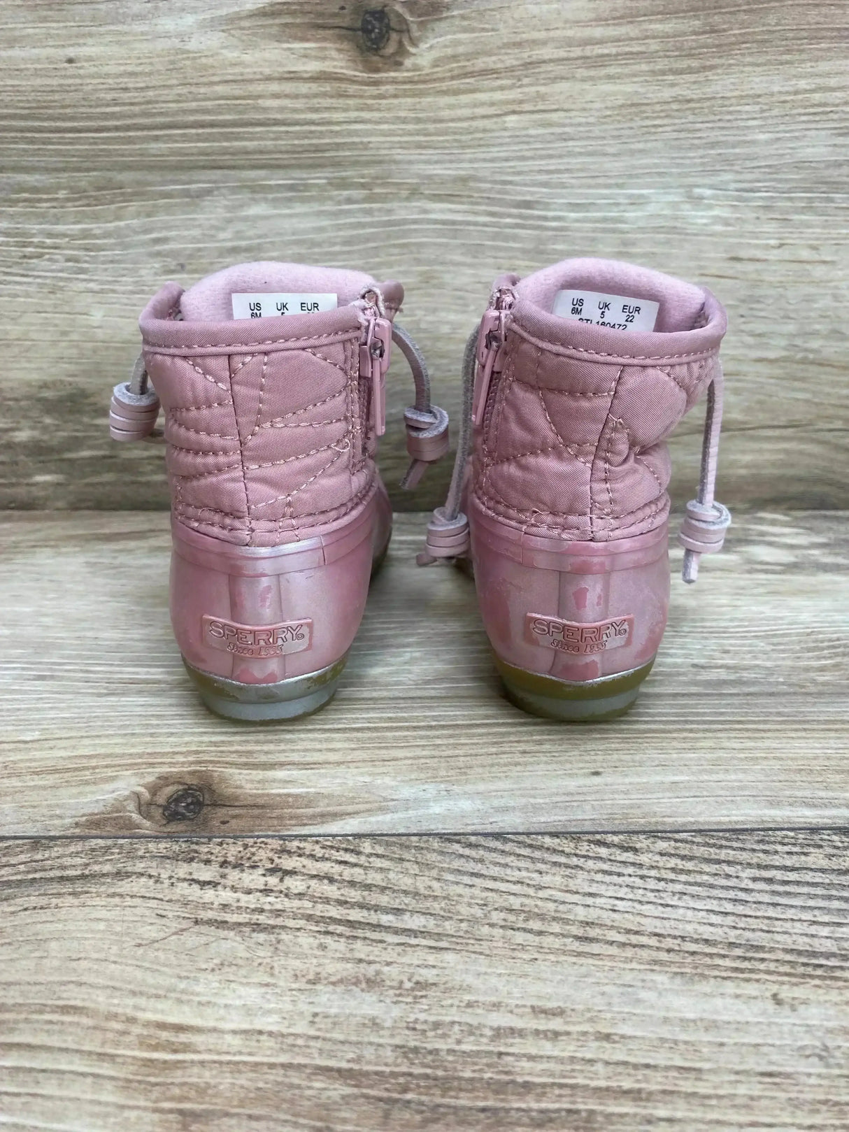 Rear view of toddler Sperry duck boots size 6C, quilted pink shafts and rubber heels with logo on wood background