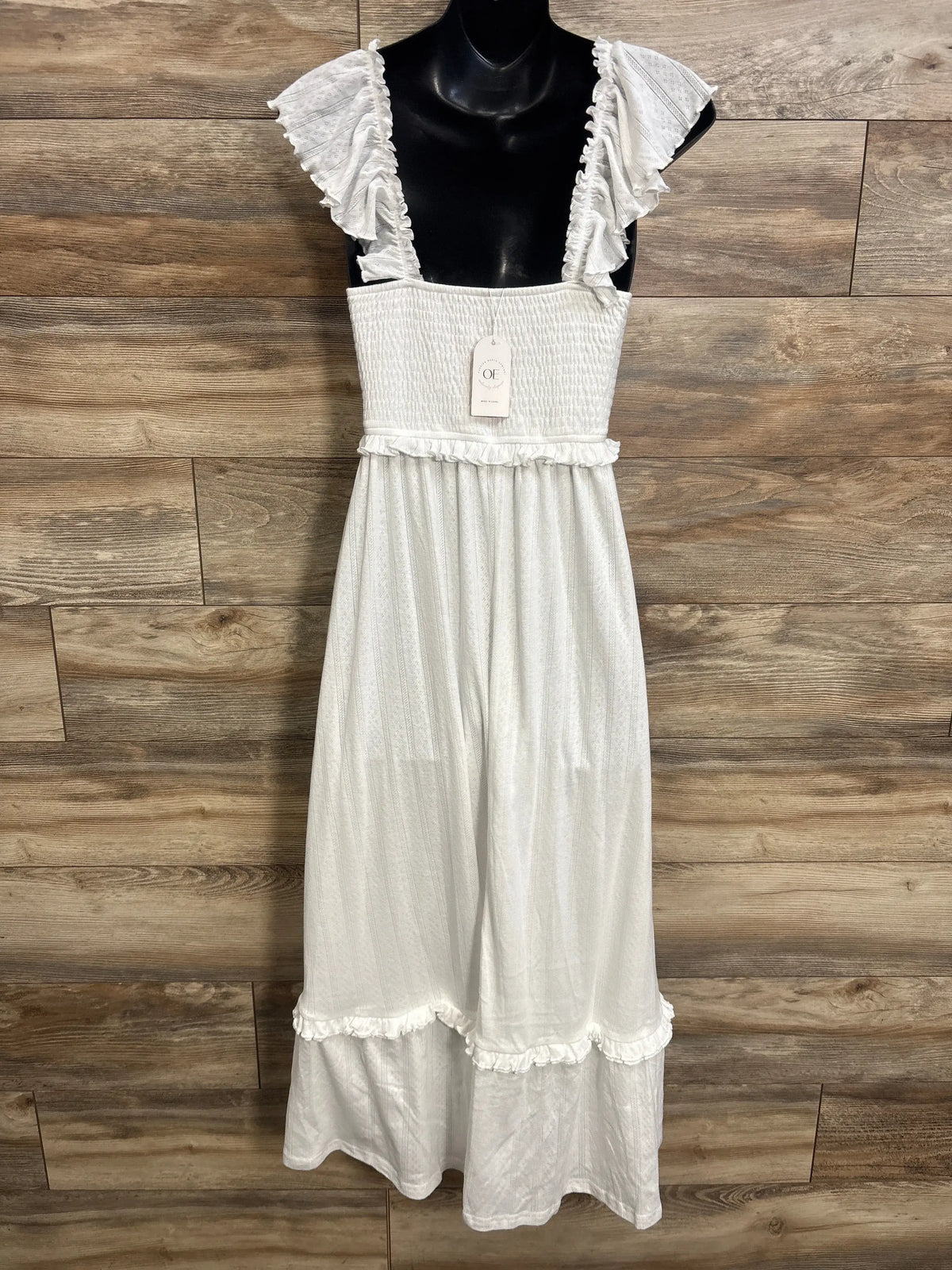 Front view of white OUGES maternity maxi dress with smocked bodice and ruffled cap sleeves against wood paneling