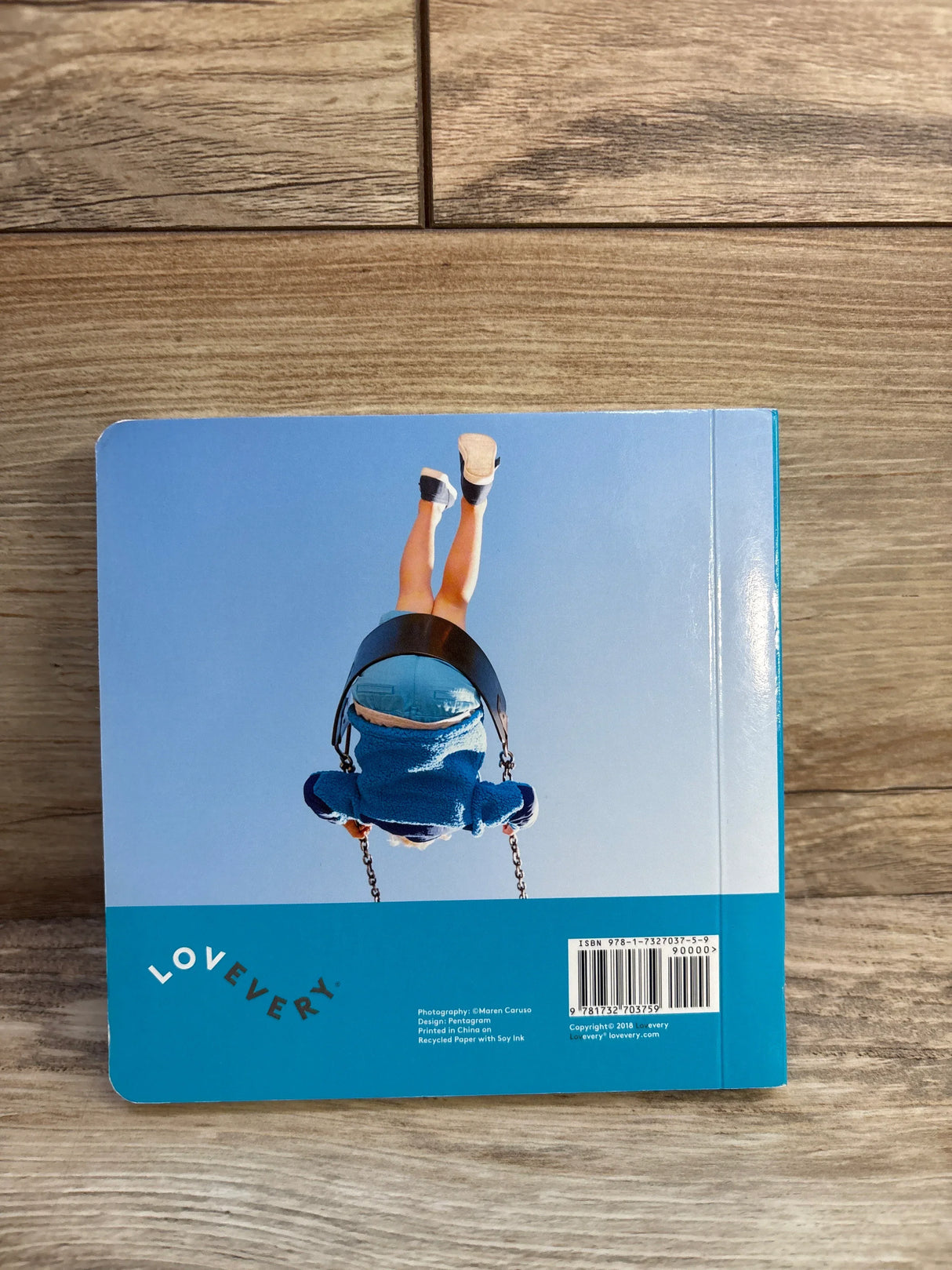 Back cover of Lovevery Max and Nana Go to the Park board book showing a child in a swing and Lovevery logo on a wood floor