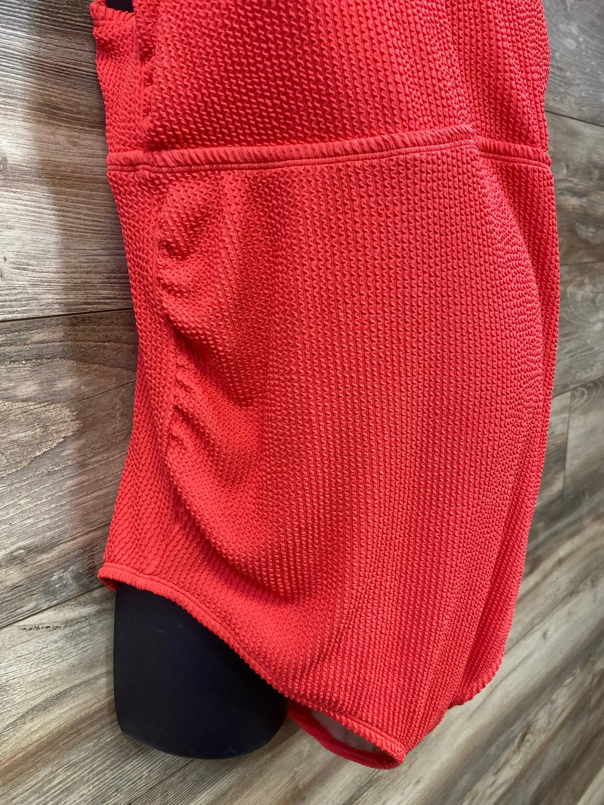 Side view of Isabel maternity one-piece swimsuit in red showing waffle texture and side ruching on wood background
