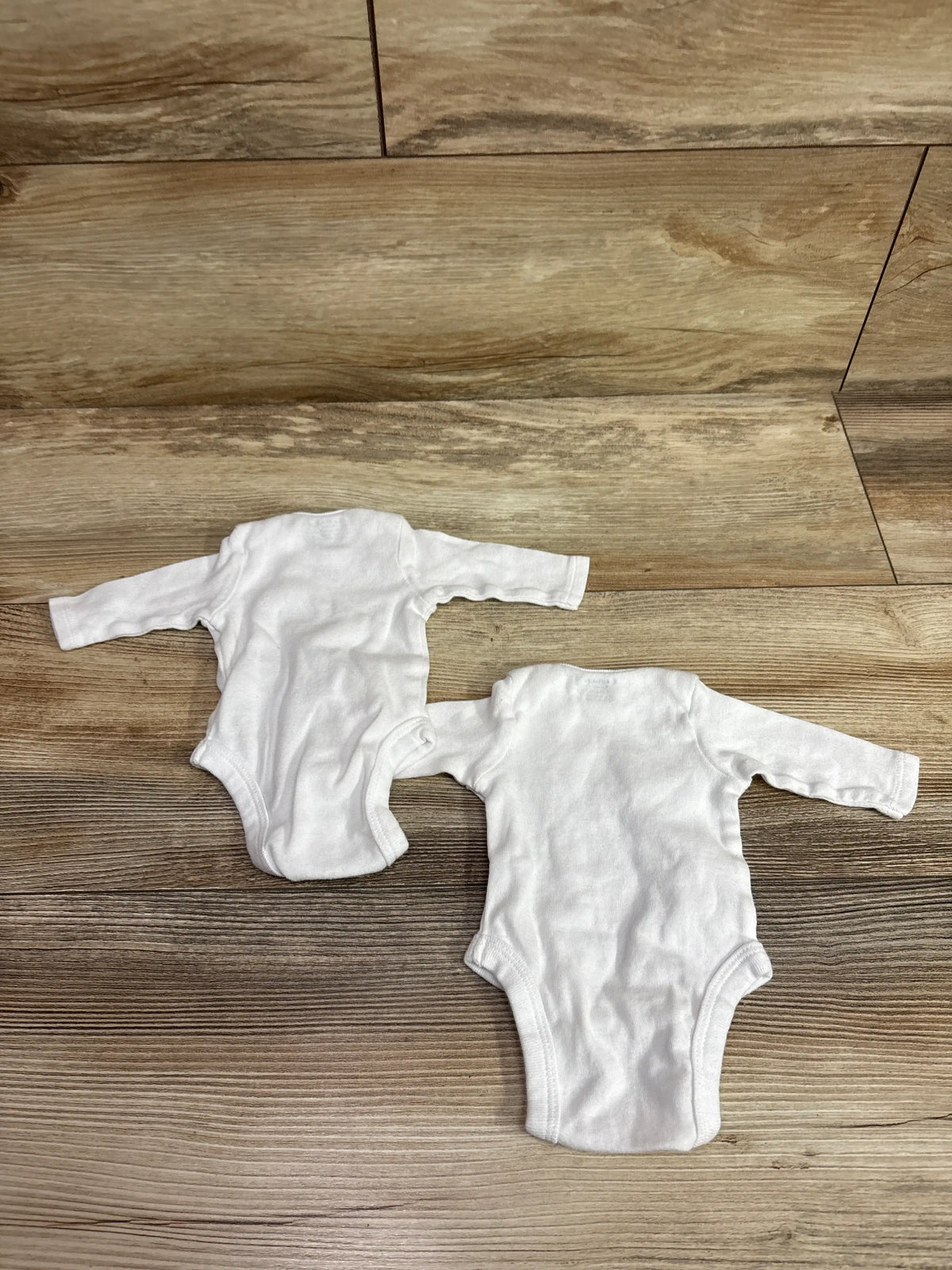 Two white Gerber long sleeve baby bodysuits in preemie size on a wood background.