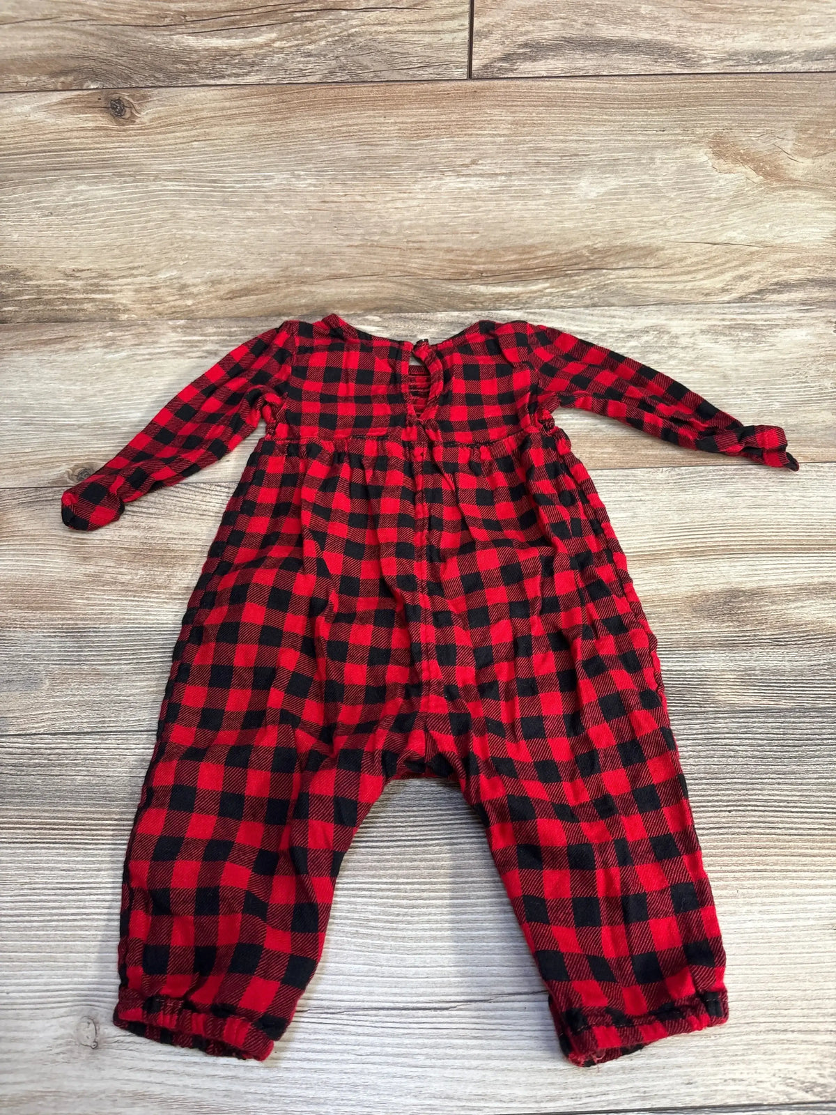 Red and black checkered baby onesie with long sleeves on wooden floor
