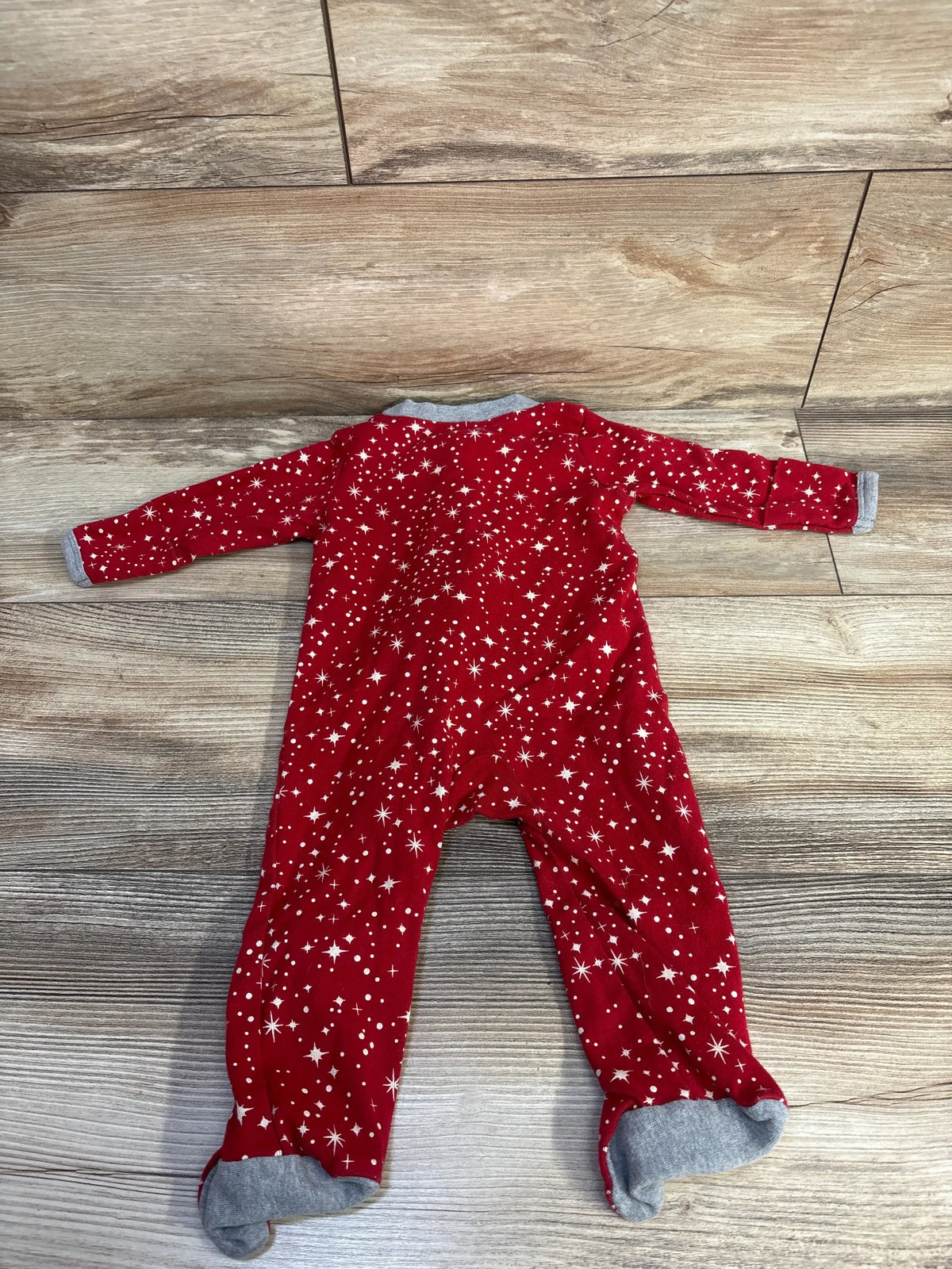 Front view of Honest Baby Star Sleeper in red with white star pattern and footed legs on a wood floor