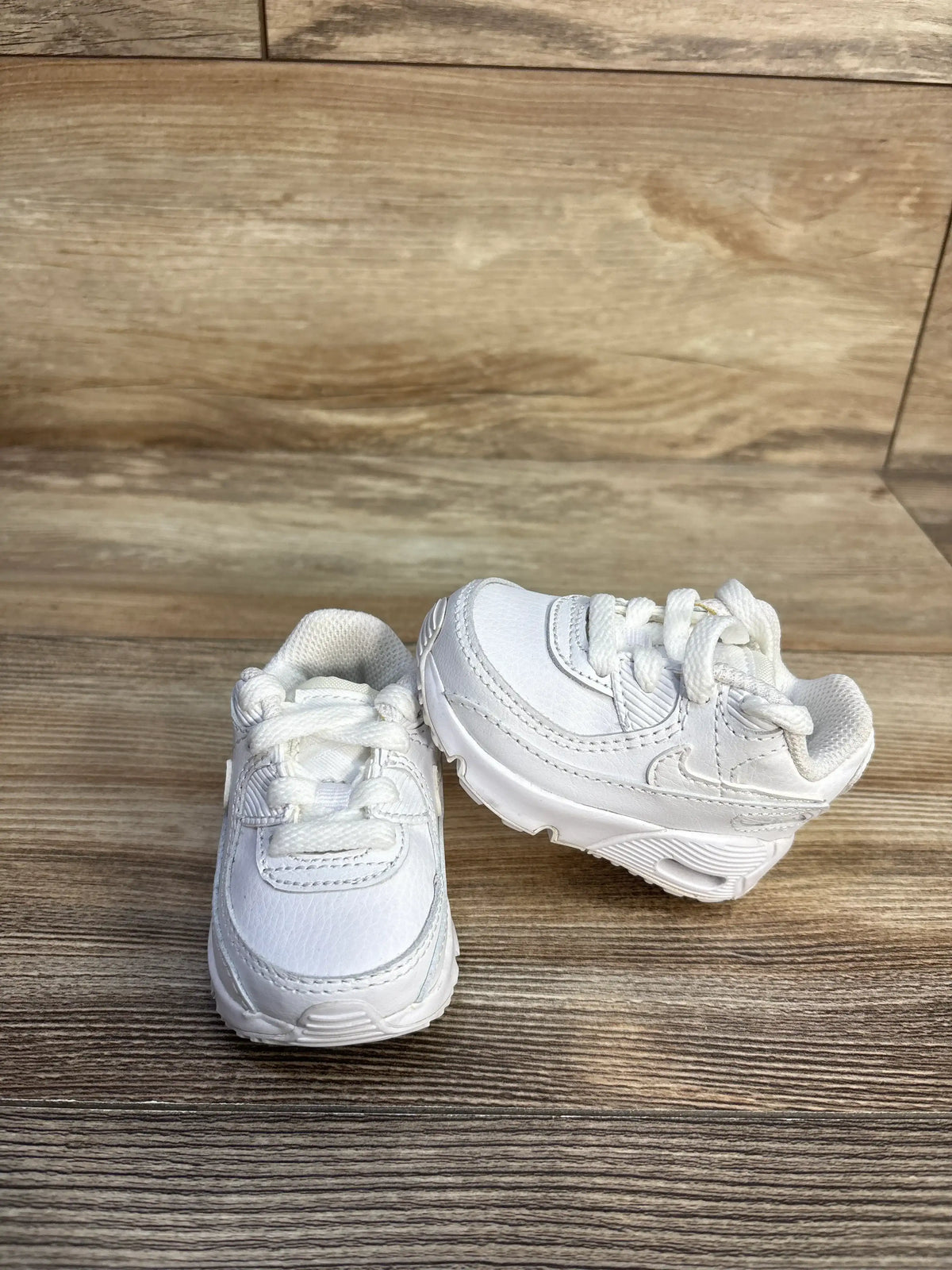 Front and side views of Nike Air Max 90 TD Triple White sneakers, size 2C, showing lace-up details on a wood floor