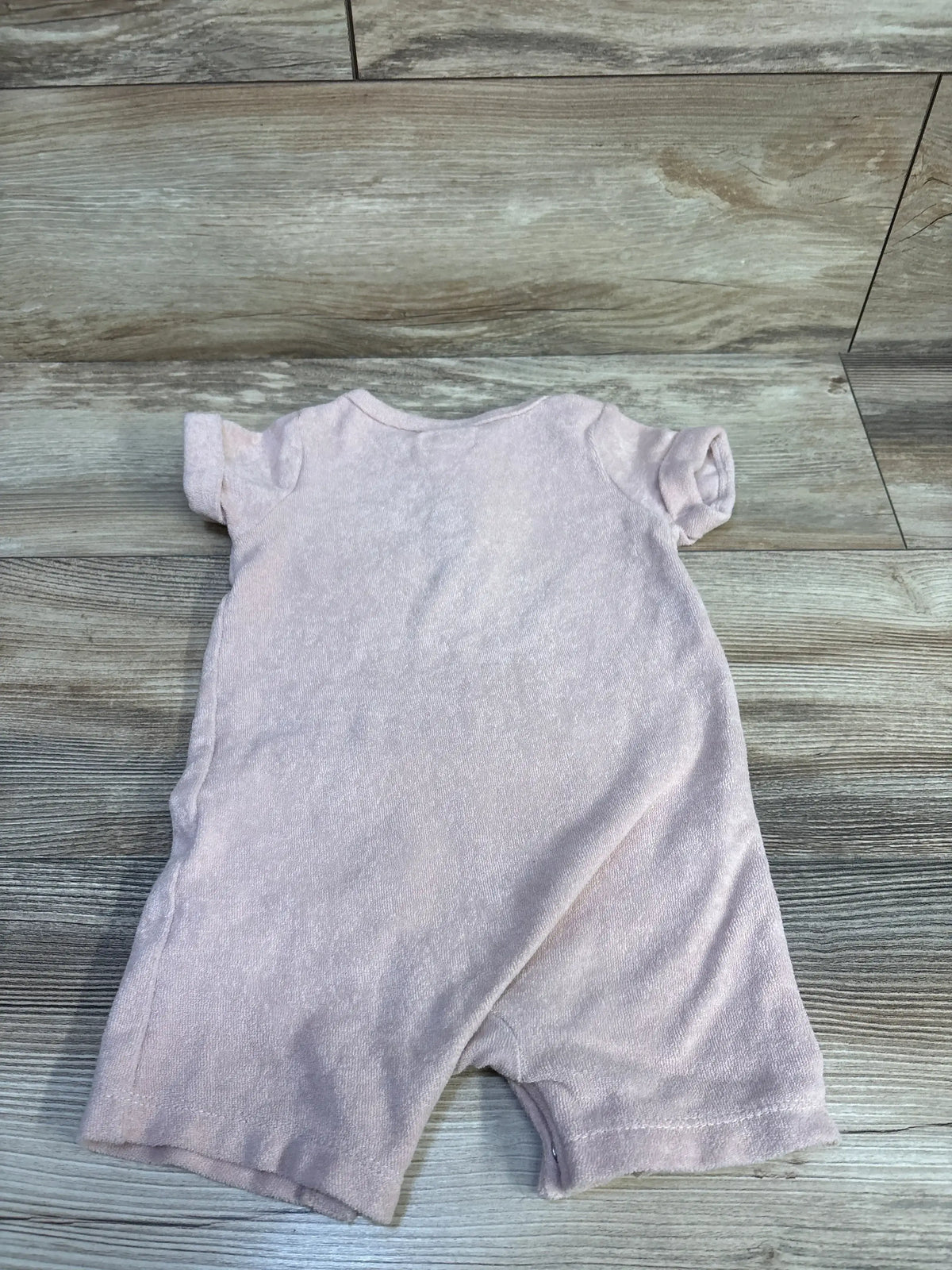 Top-down view of pink terry cloth romper (12 months) showing short sleeves and short legs, back-facing on wood floor