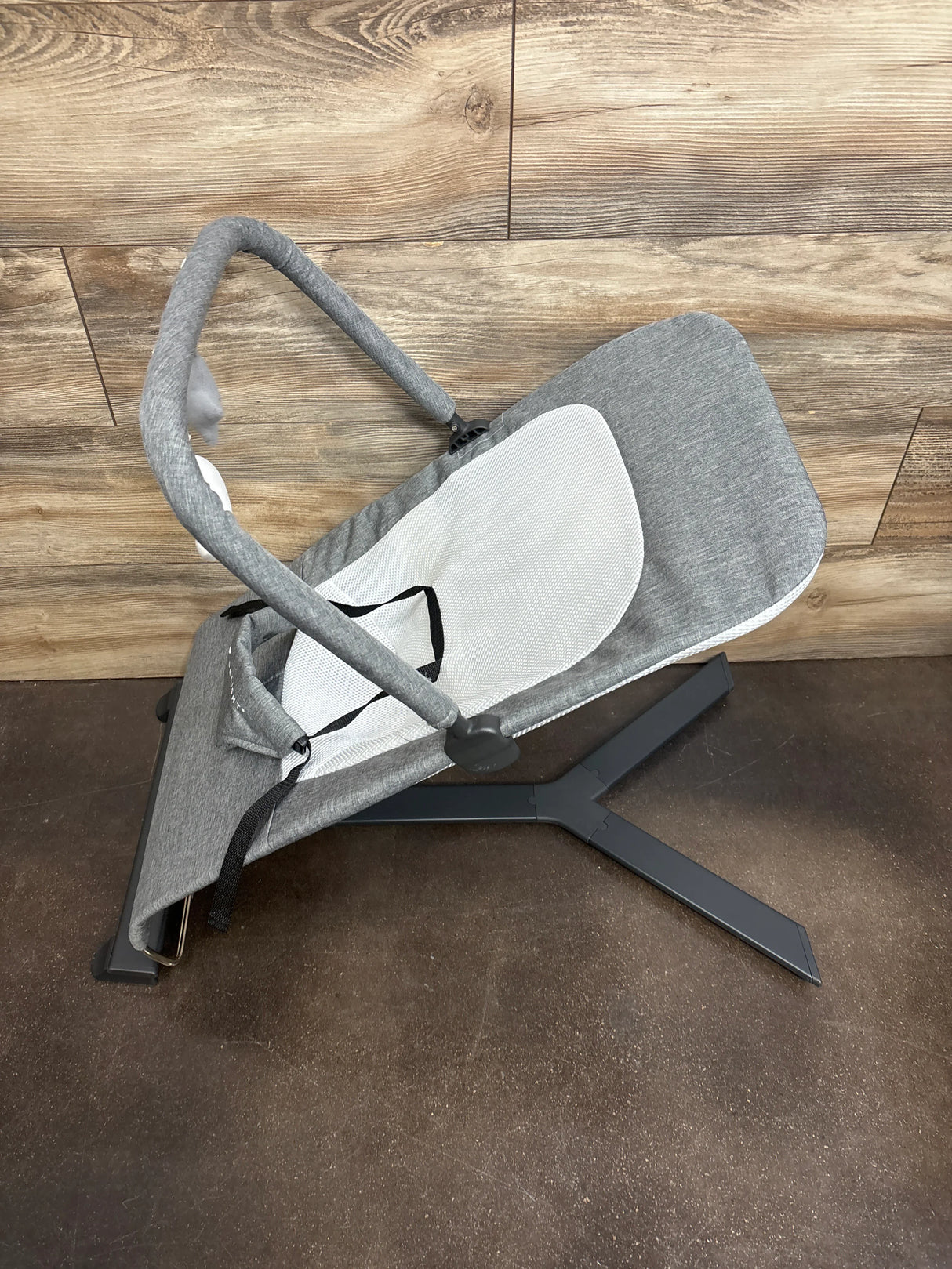 Side view of Baby Delight Alpine Deluxe Bouncer in charcoal grey showing mesh seat insert, removable toy bar, and black metal X-base on wood floor