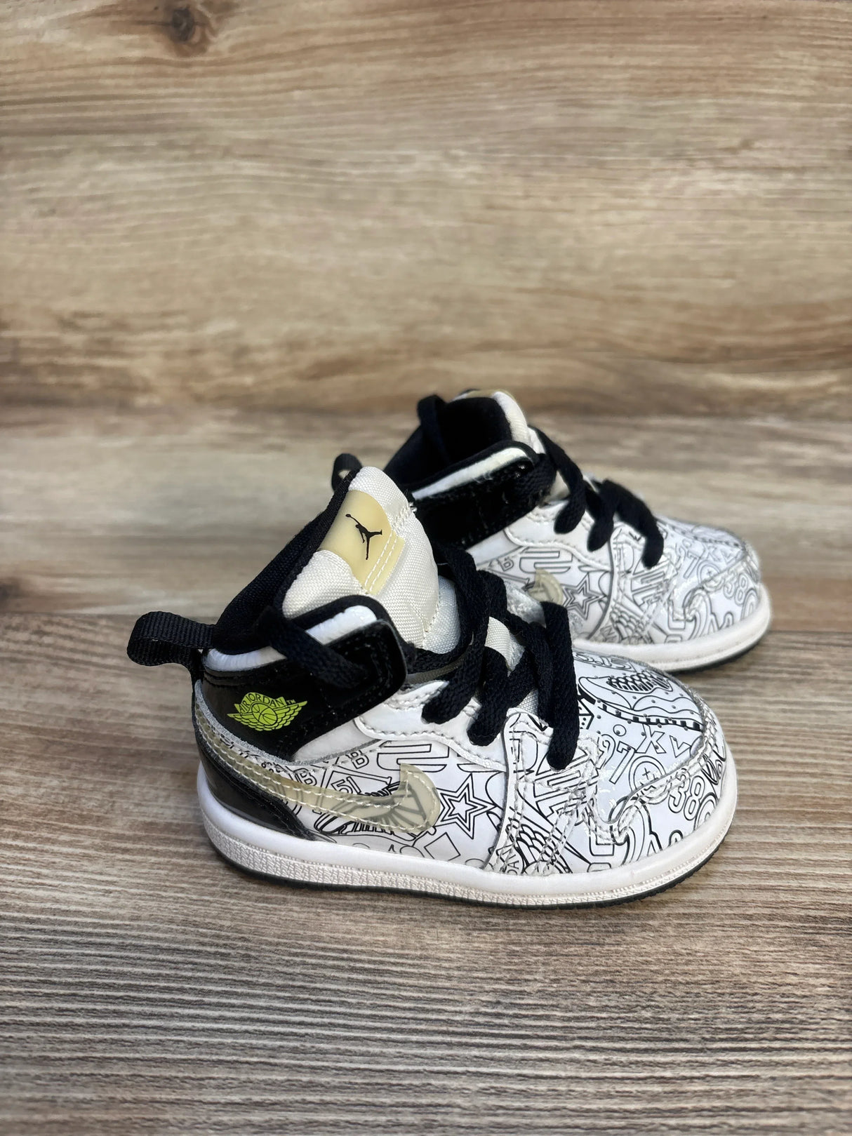 White and black toddler Jordan sneakers with graphic pattern and yellow logo on wood surface