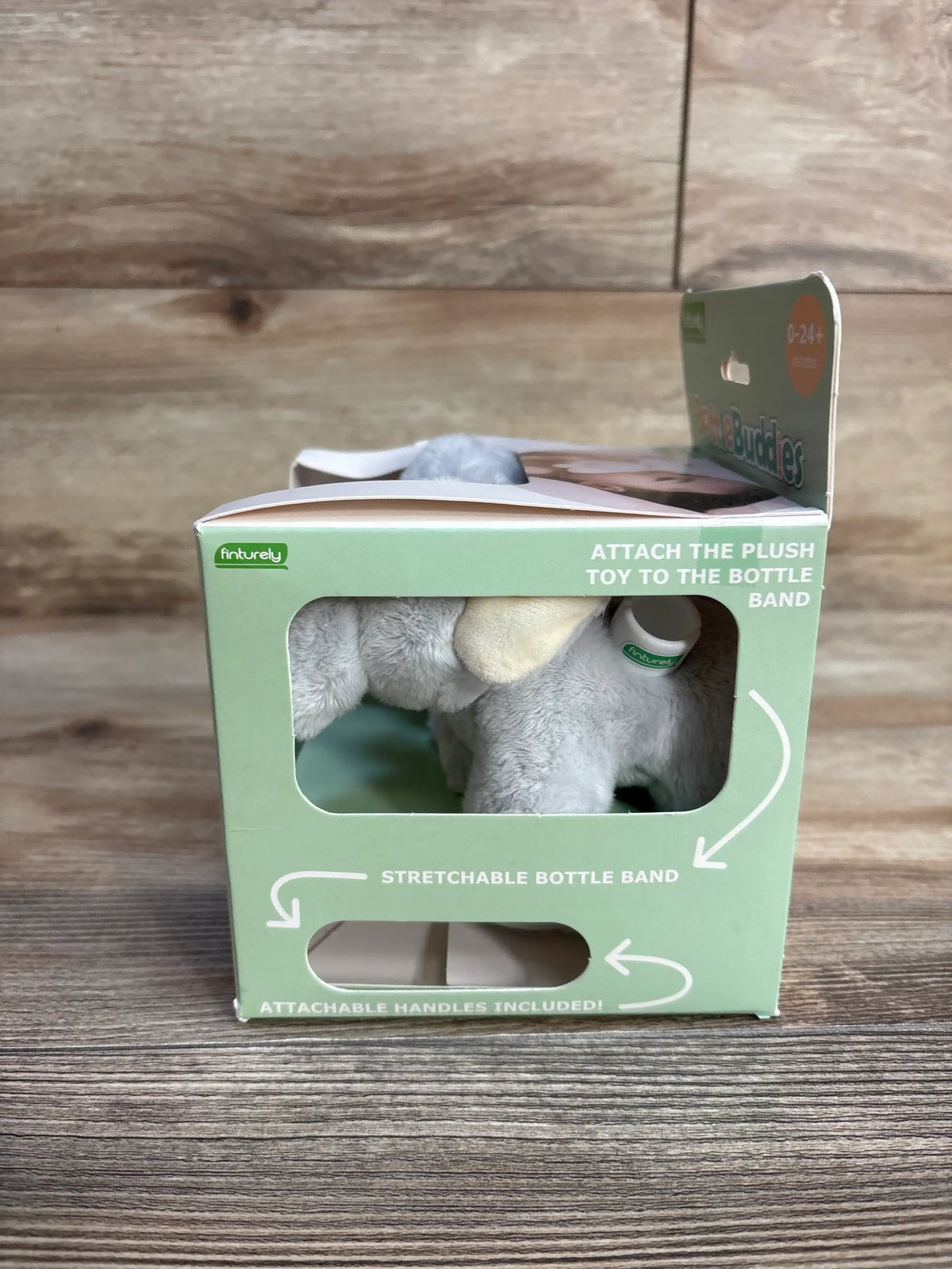 Front view of Bottle Buddies elephant starter kit showing elephant through packaging window of green box on wood background