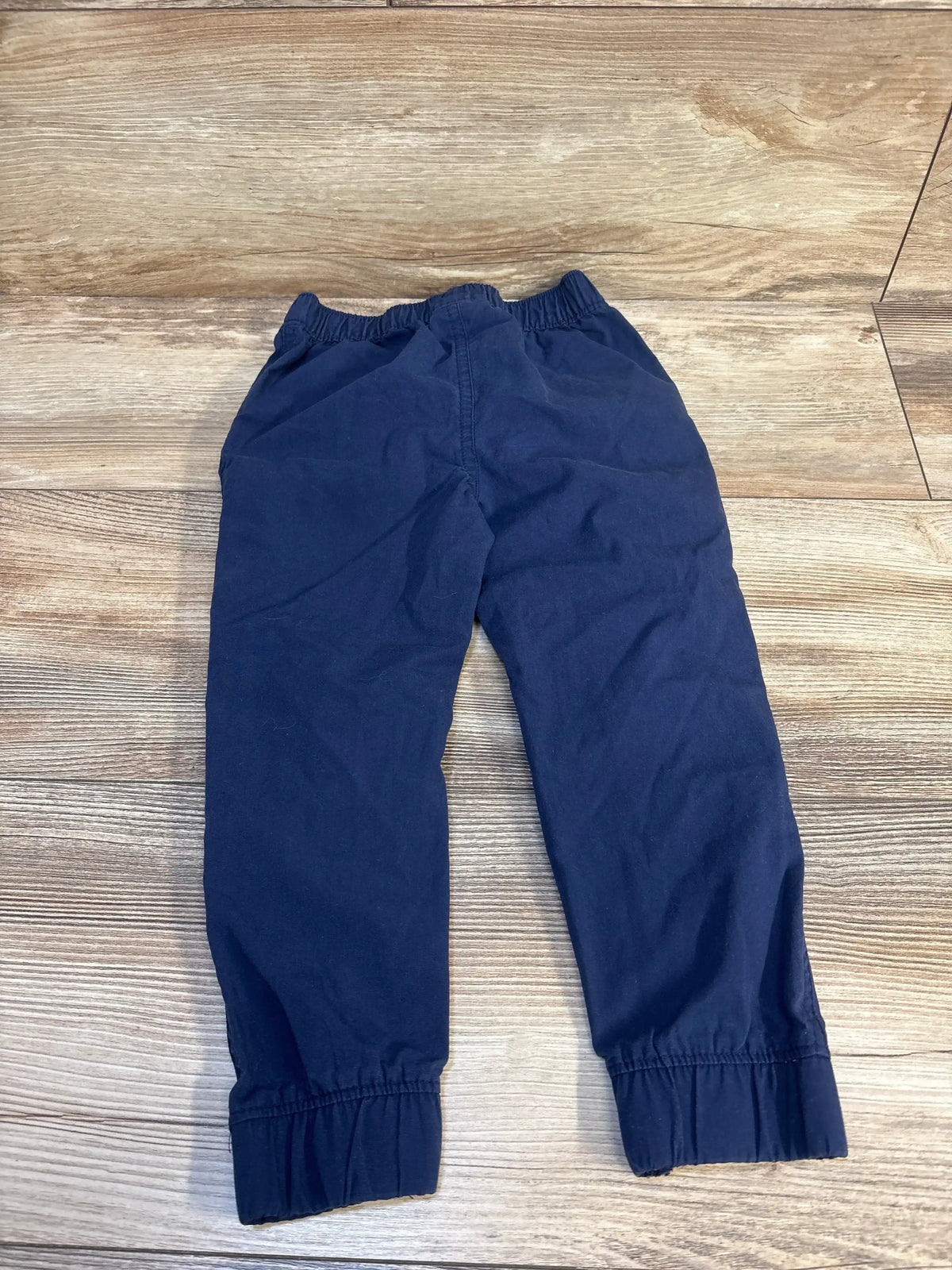 Navy blue kids joggers with elastic waist and cuffs, laid flat on wood floor