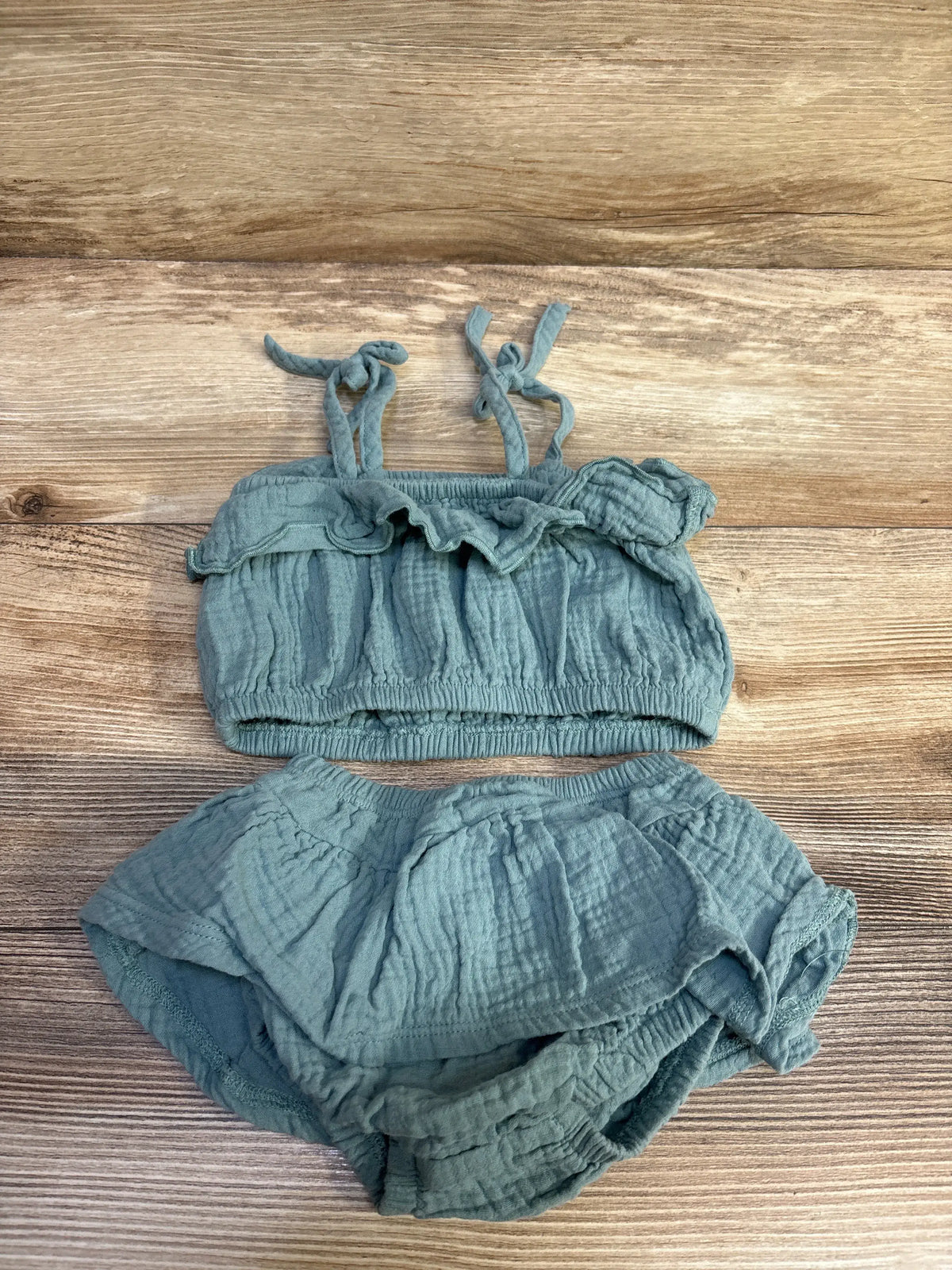 Top down view of green gauze tank top and bloomers set showcasing tie straps and ruffled trim on a wood background