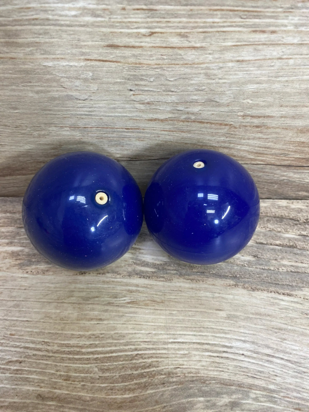 Top-down view of Lovevery Opposite Balls Blue showing two blue plastic balls with small valve holes on a wood surface