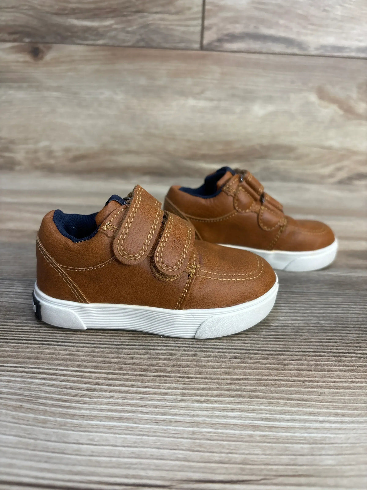 Brown toddler shoes with velcro straps, navy lining, white soles on wood floor
