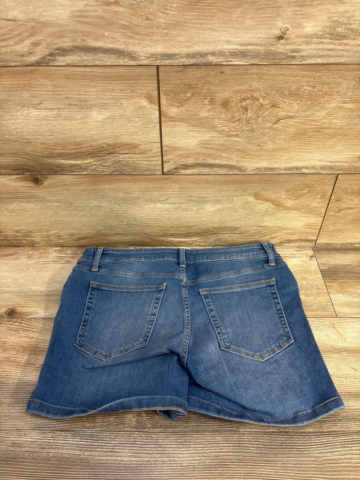 Rear view of Gap maternity denim shorts showcasing two functional back pockets and a medium wash blue finish on a wood floor