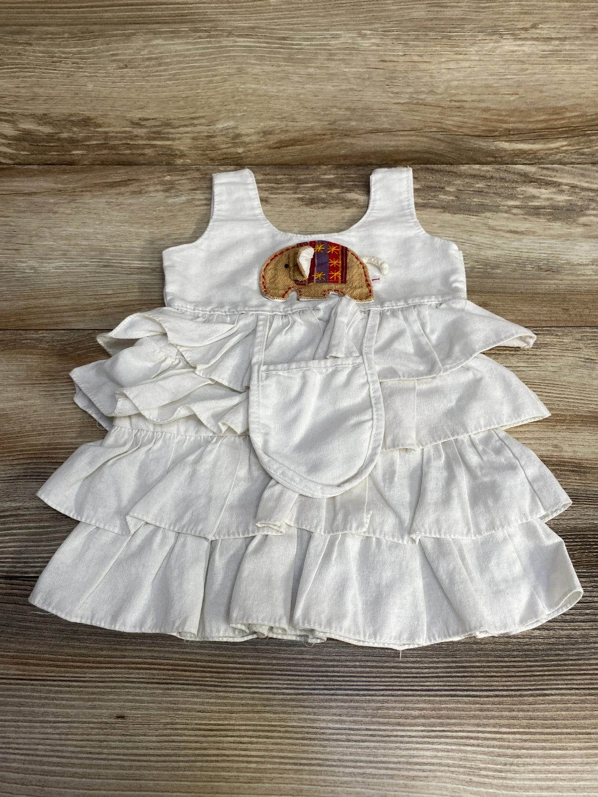 Flat lay of white tiered baby dress (3-6M) with embroidered elephant applique and layered ruffle skirt on wood background