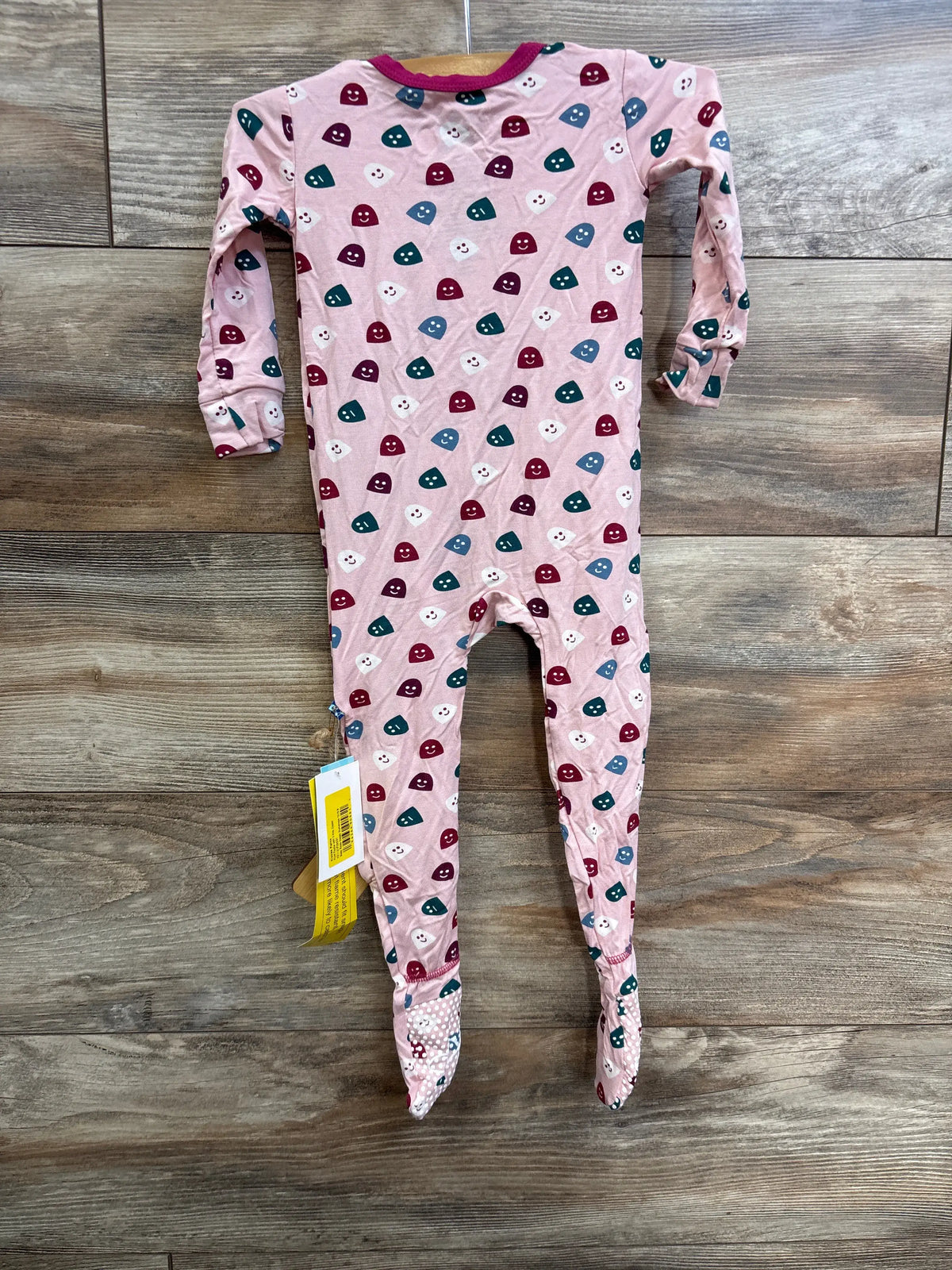 Front view of Kickee Pants Happy Gumdrops pink zip footie with long sleeves, feet, and colorful print on wood