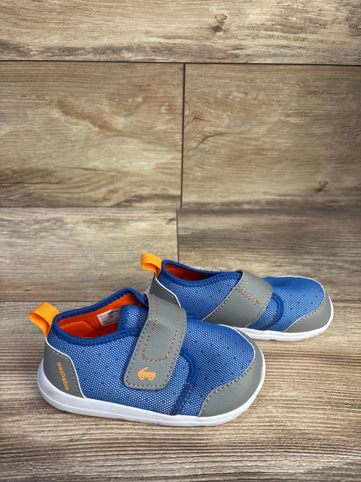 Side view of See Kai Run Ryder toddler FlexiRun water shoes, blue with gray strap and orange pull tab on wood background