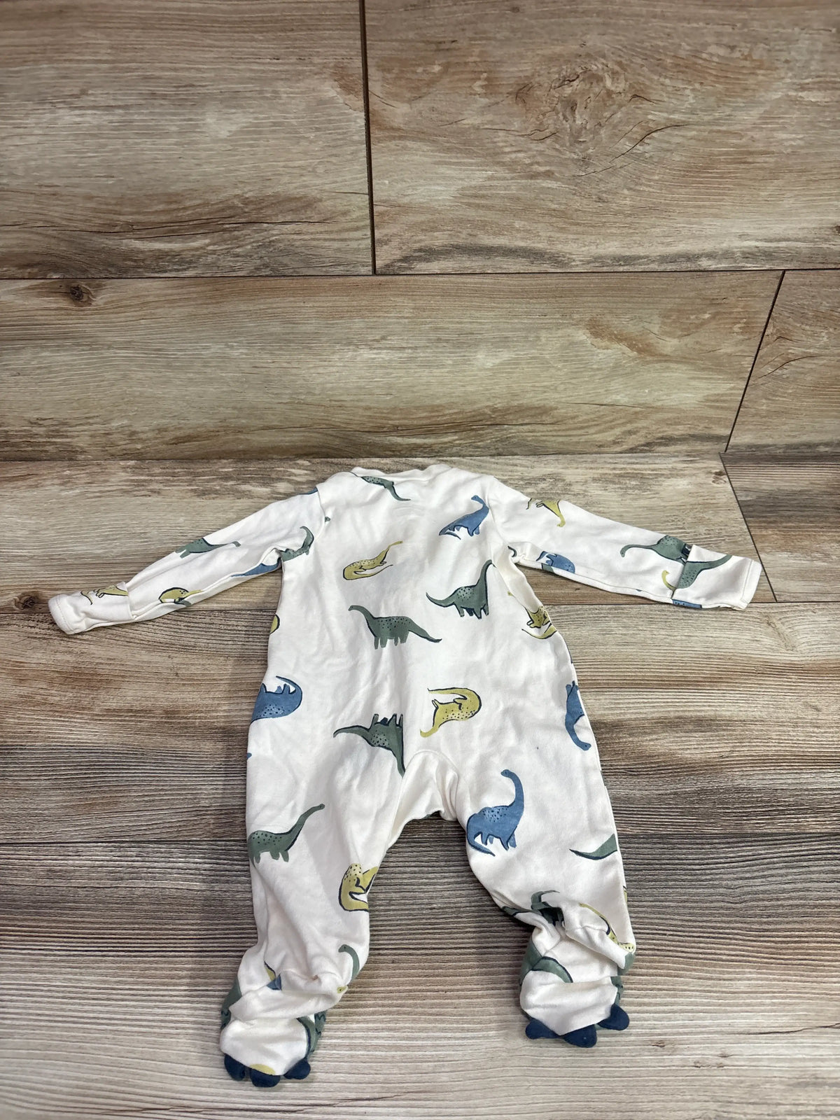 Top view of Child Of Mine sleeper showcasing dinosaur print, long sleeves, and footed design on a wood floor