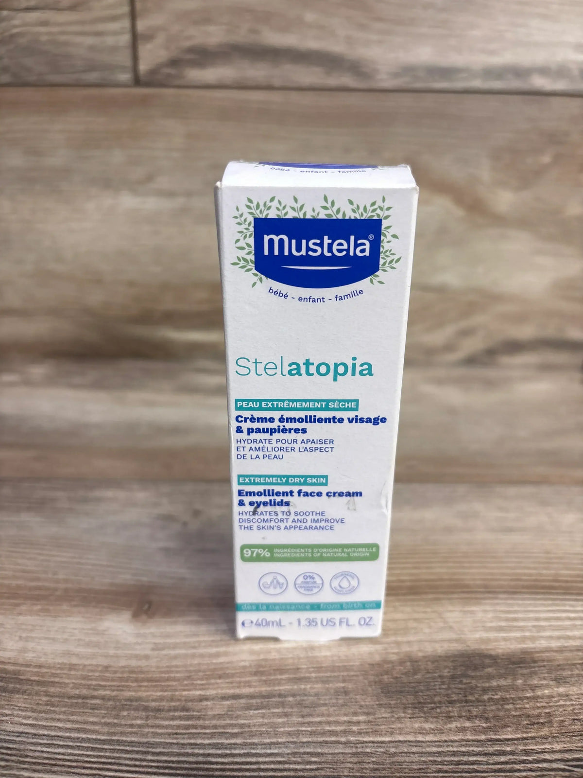 Front view of Mustela Stelatopia emollient face cream box showing label Emollient face cream and eyelids 40 mL wood surface