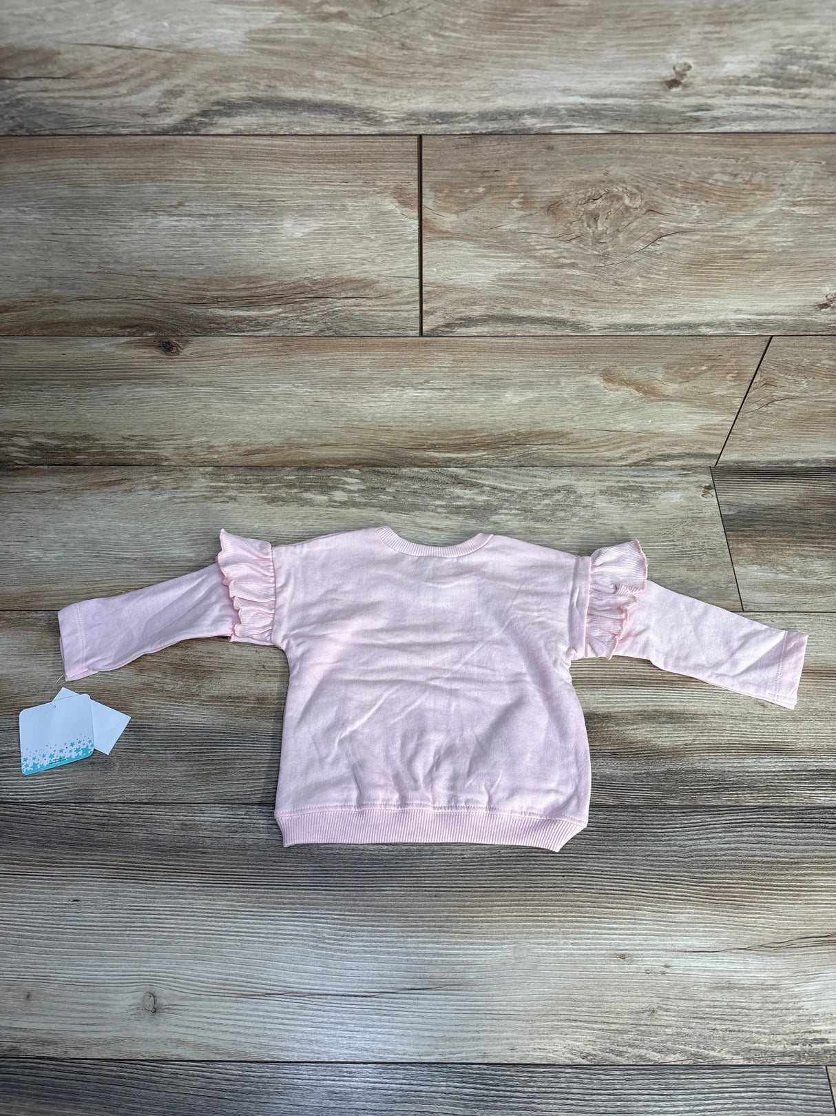 Back of pink Disney Baby Minnie Mouse sweatshirt showcasing ruffled shoulder detail with wood plank background