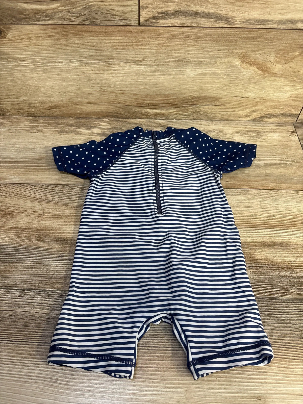 Flat lay of 18M striped rashguard swimsuit with front zipper, navy and white stripes and navy polka dot sleeves on wood floor