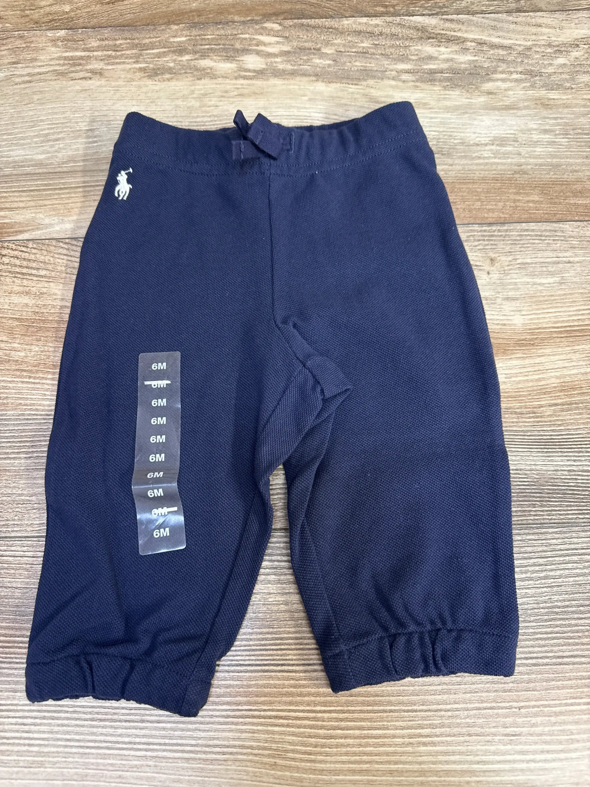 Front view of navy Ralph Lauren baby sweatpants (6M) showing elastic waistband, elastic cuffs, embroidered white Polo logo on wood background