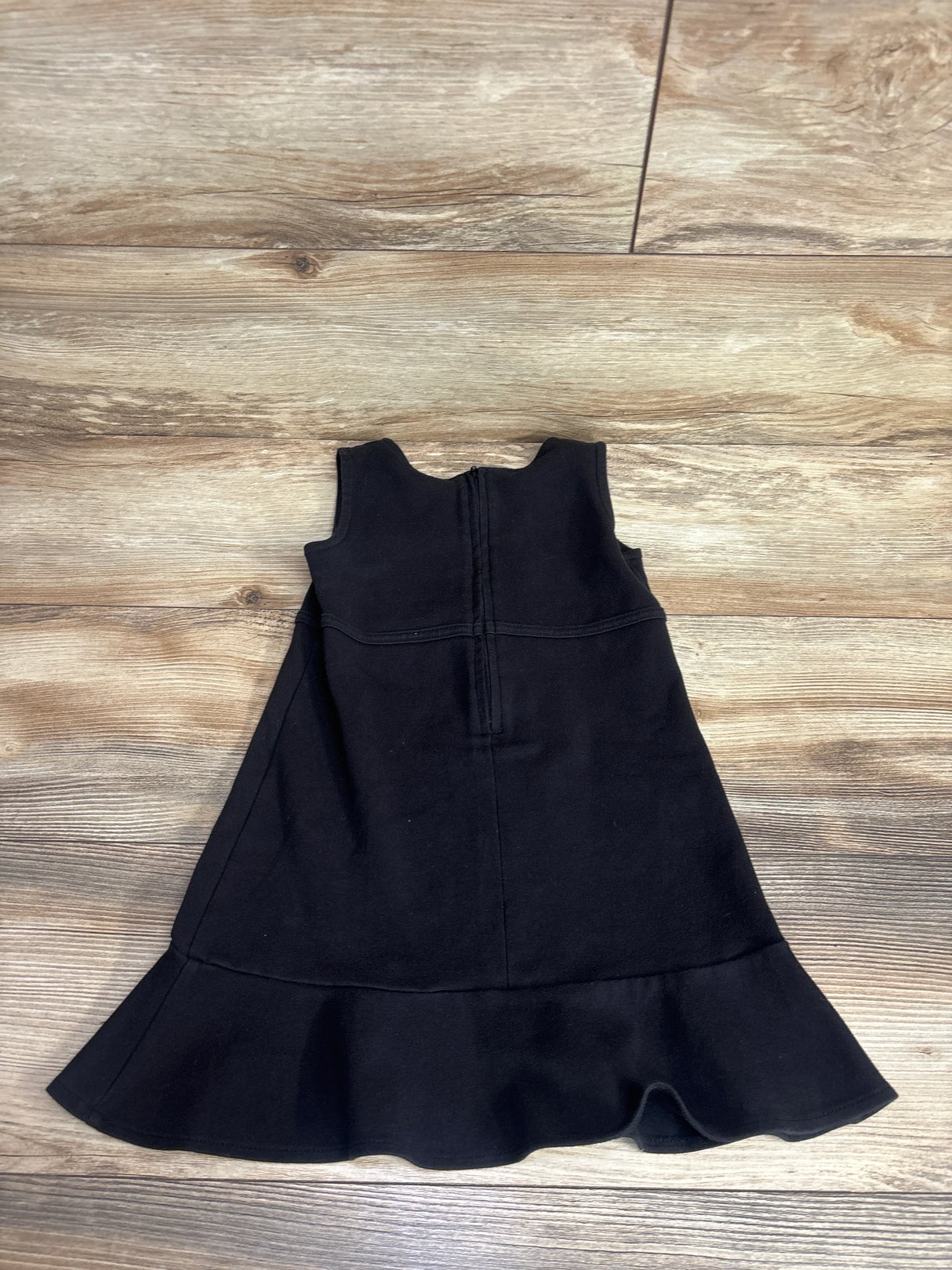 Black sleeveless girls dress with ruffled hem, laid flat on wooden floor, kids clothing
