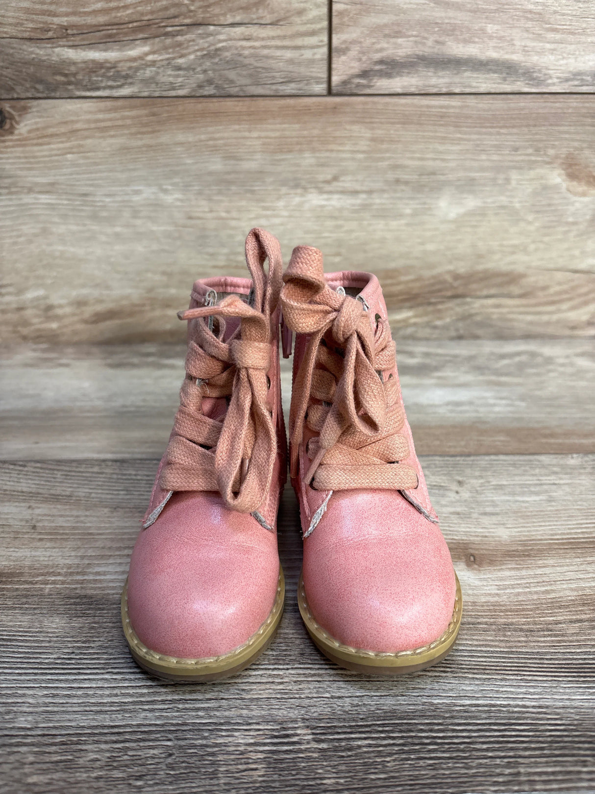 Pair of pink kids lace-up boots on wooden floor with light brown sole