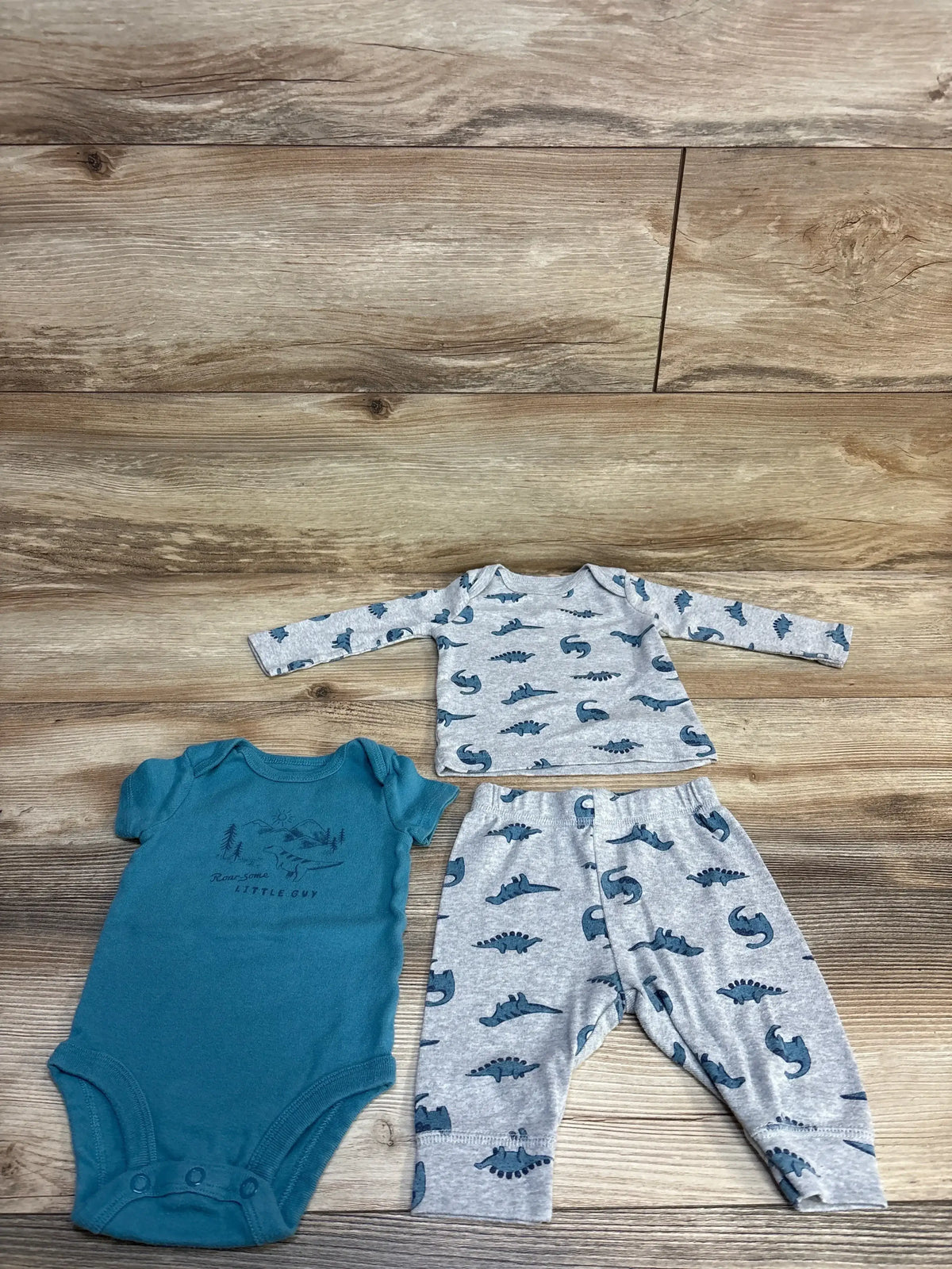 Baby boy outfit set with teal onesie, dinosaur print shirt and matching pants on wood background