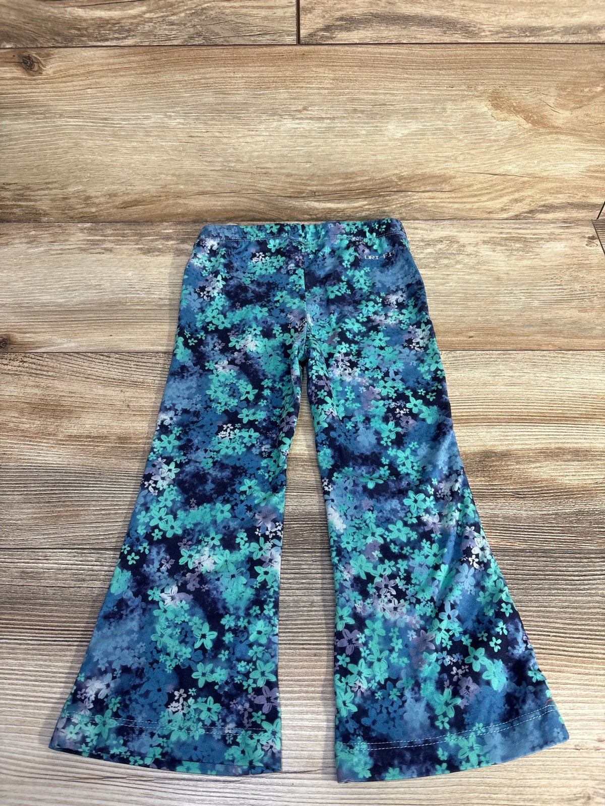 Front view of Nike Dri Fit floral flared leggings showcasing the blue floral print and flared legs on a wood floor