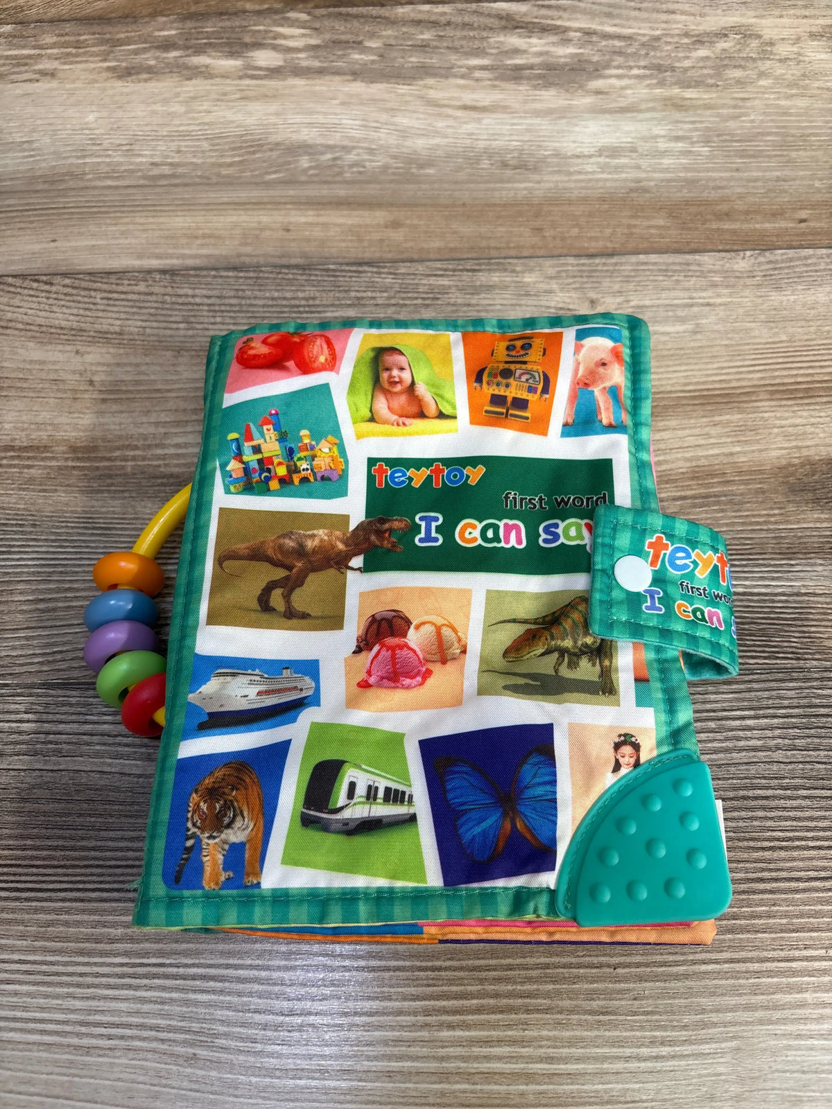 Front view of Teytoy First Word I Can Say Soft Activity Book with colorful images and teether tabs on a wood surface
