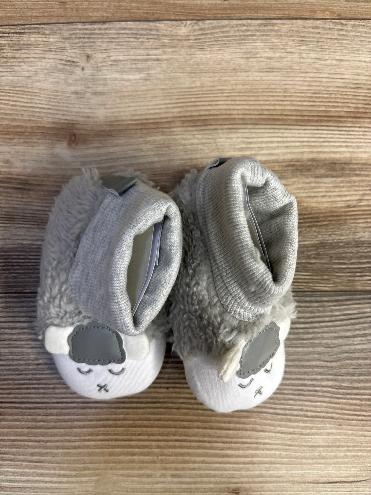 Soft gray baby booties with sheep face design on wooden background
