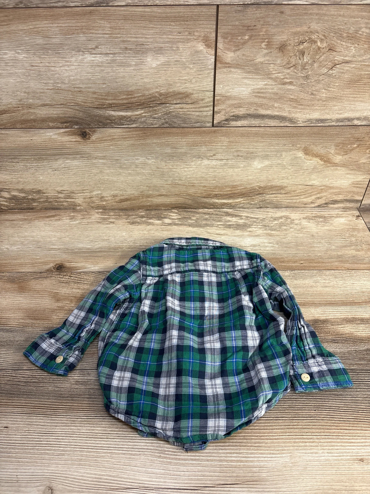 Green and blue plaid baby shirt with long sleeves on wood background