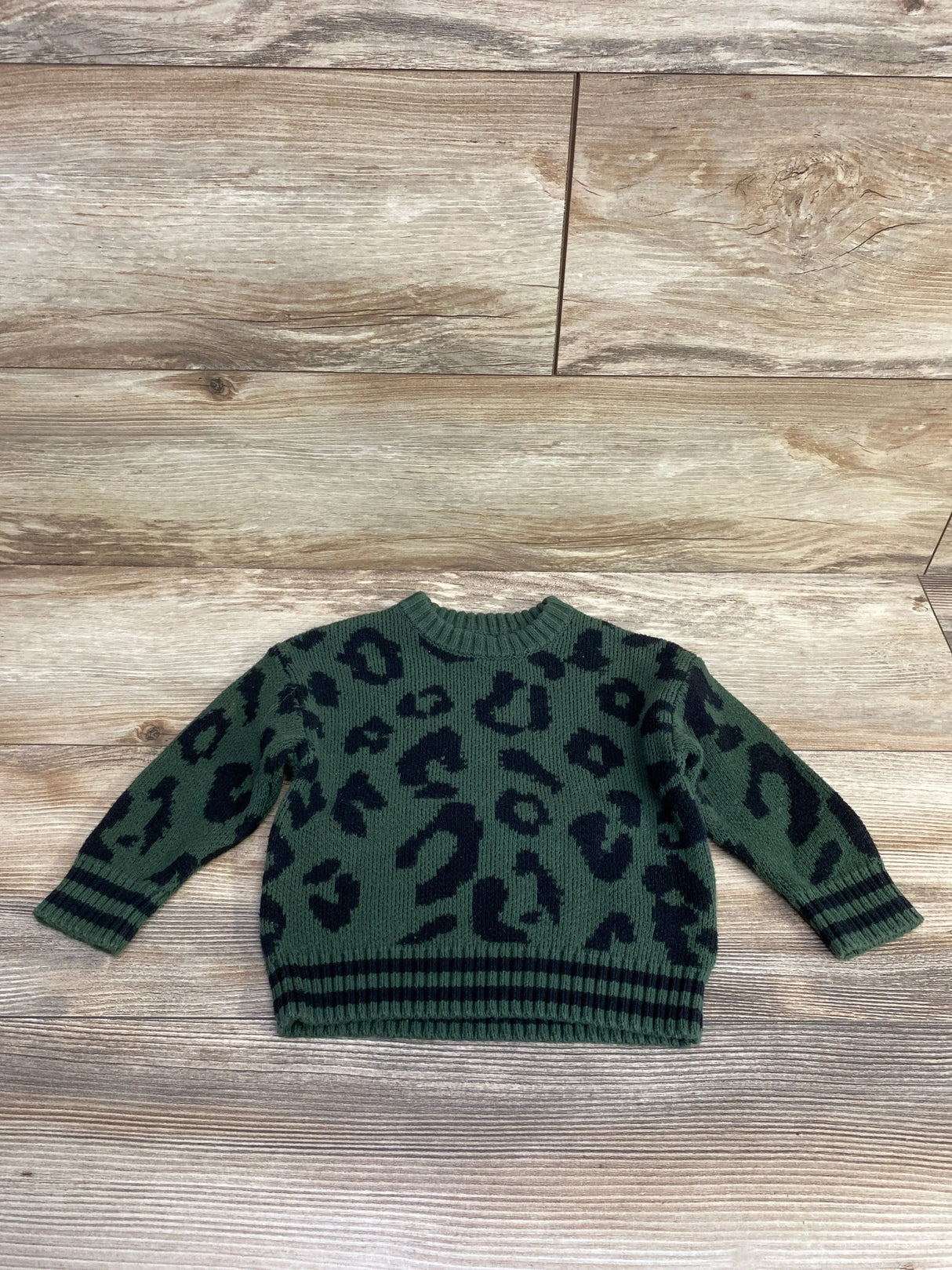 Green kids sweater with black leopard print, long sleeves, ribbed cuffs and hem on wood floor