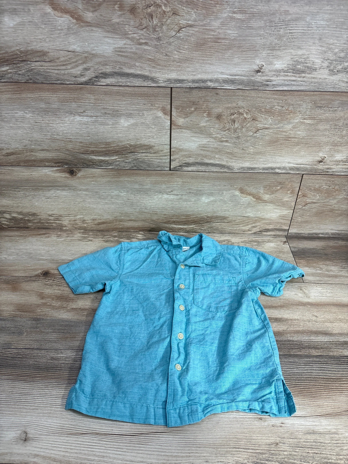 Light blue short sleeve boys button up shirt with chest pocket on wood background