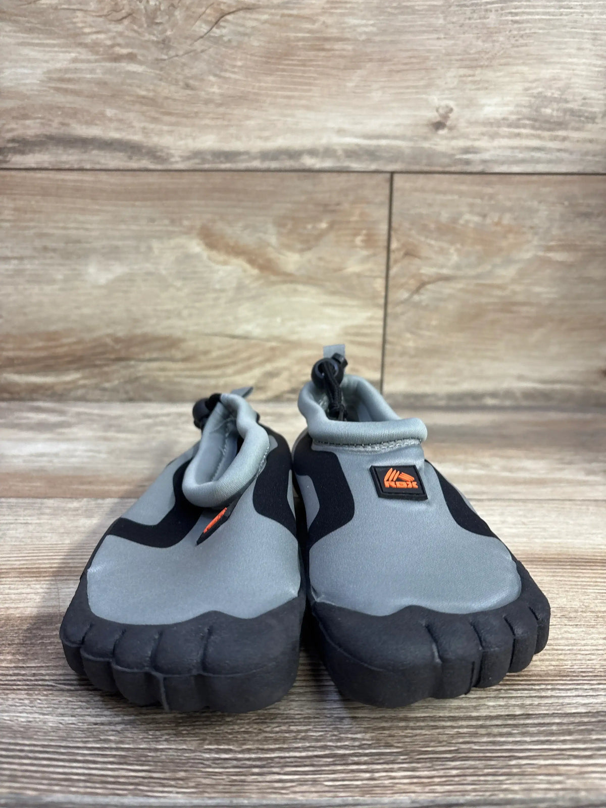 Front view of RBX toddler water shoes showcasing gray neoprene uppers and black segmented rubber sole on wood floor