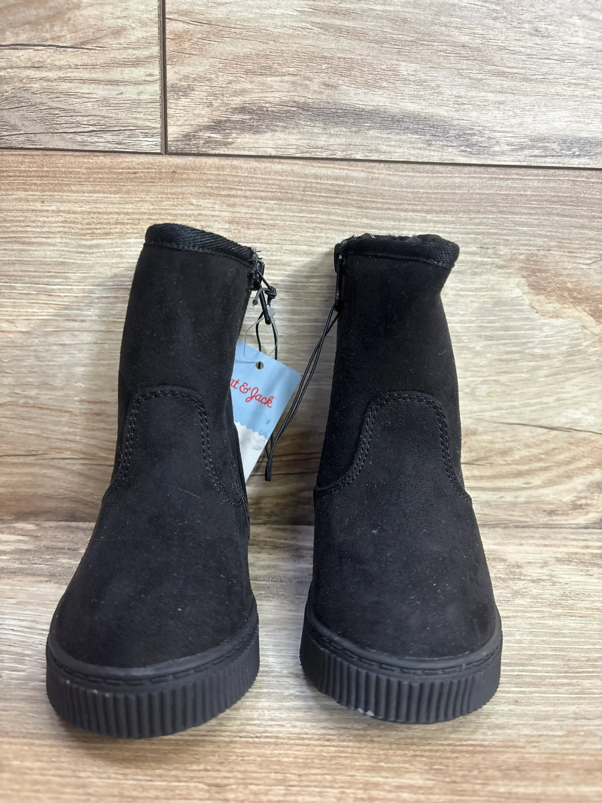 Pair of black suede children’s boots with side zipper on wood floor