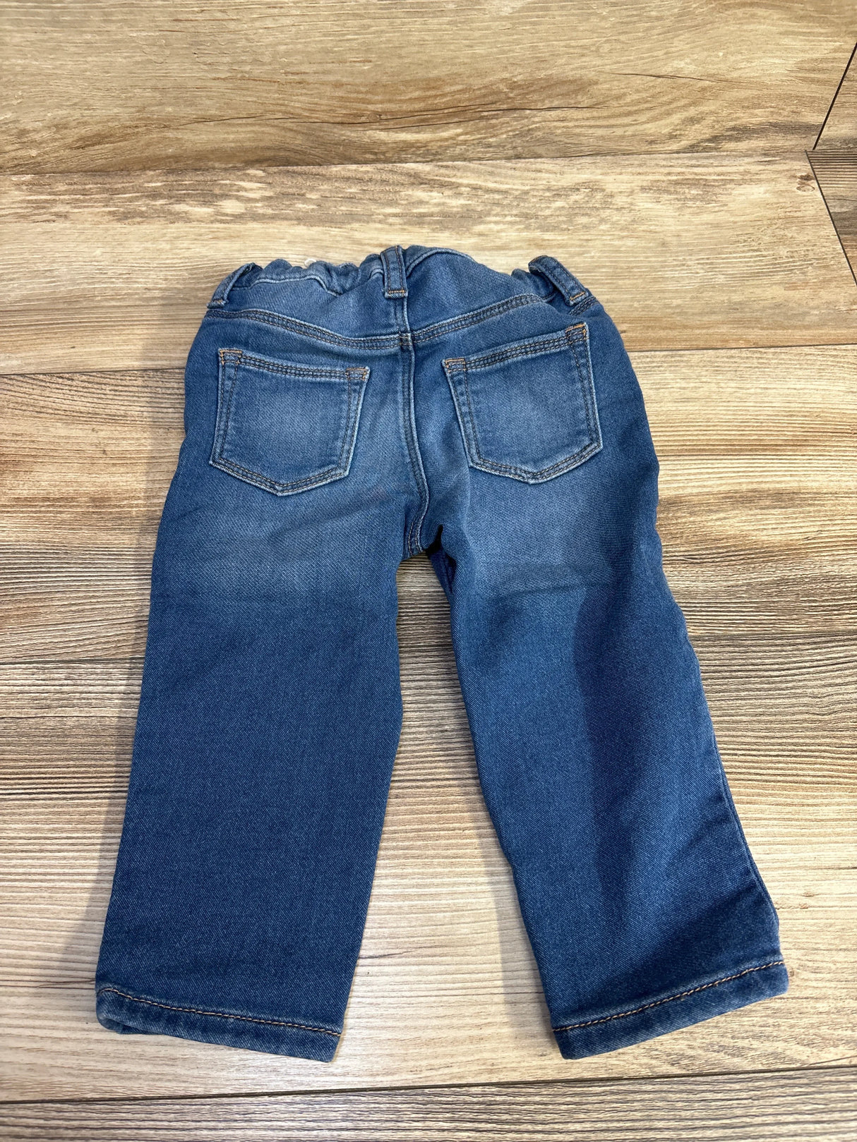 Back view of H&M toddler denim pants, size 12M, showing elastic pull-on waist and two back patch pockets on wood floor