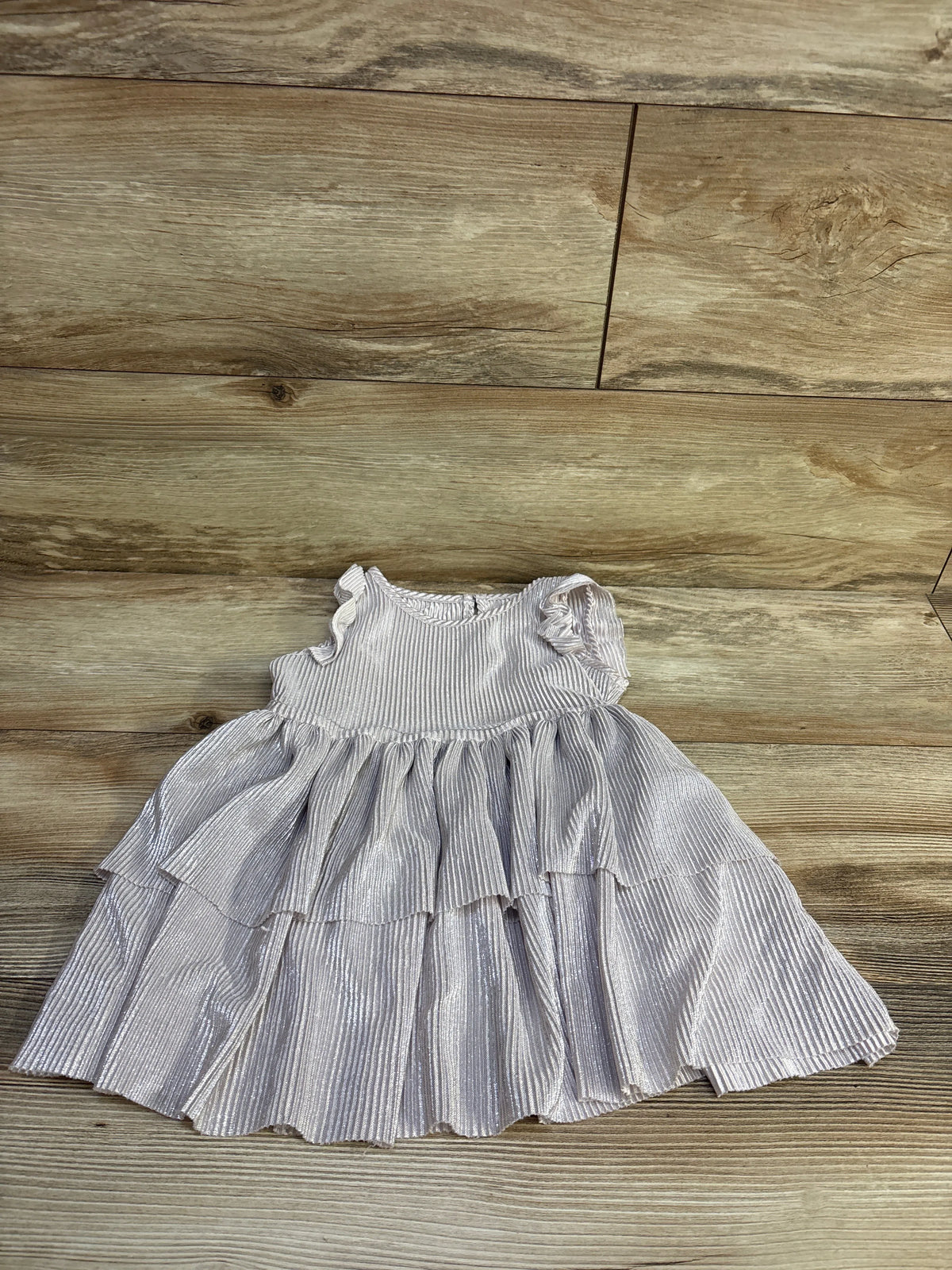 Top-down view of Biscotti metallic toddler dress with silver shimmer, tiered ruffle skirt and cap sleeves on light wood floor