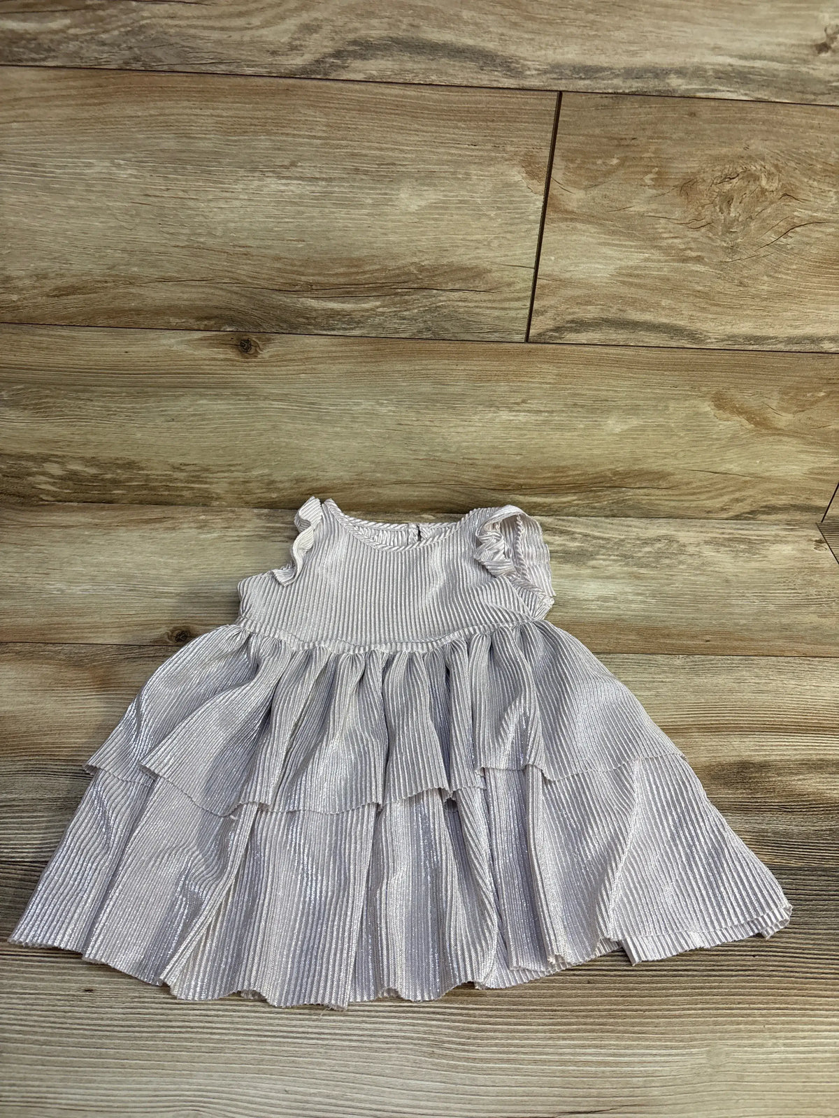 Top-down view of Biscotti metallic toddler dress with silver shimmer, tiered ruffle skirt and cap sleeves on light wood floor