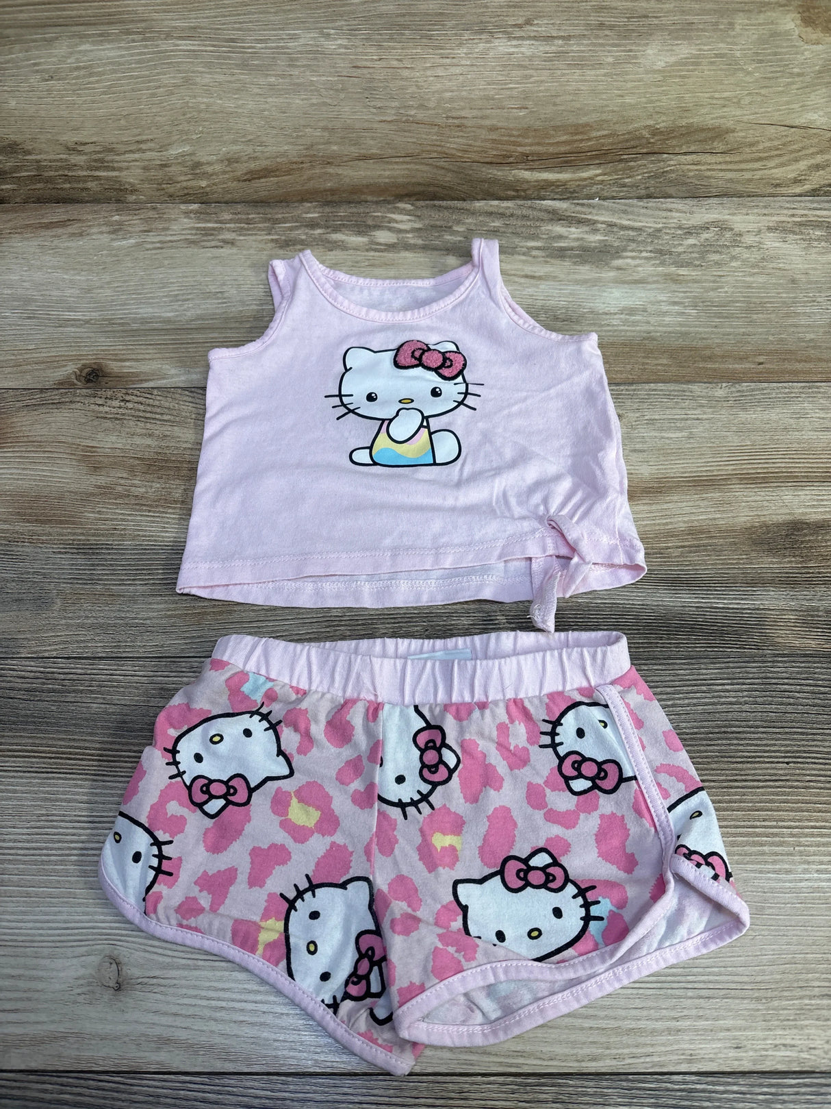 Flat lay of pink Hello Kitty tank top and shorts showing front print and elastic waistband on wood background