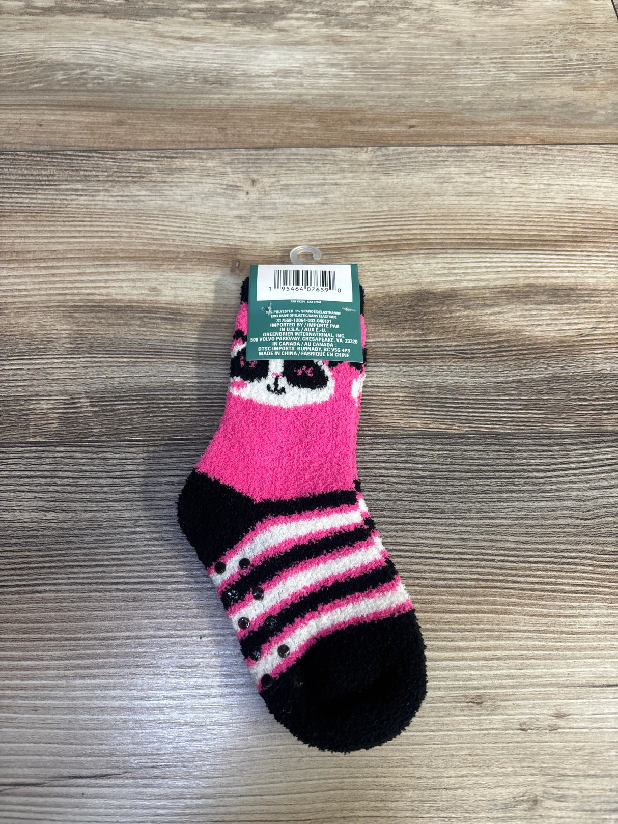 Top-down view of a pink Snugadoo kids fuzzy sock showing panda face, black-and-pink stripes and non-slip grip dots on a wood surface