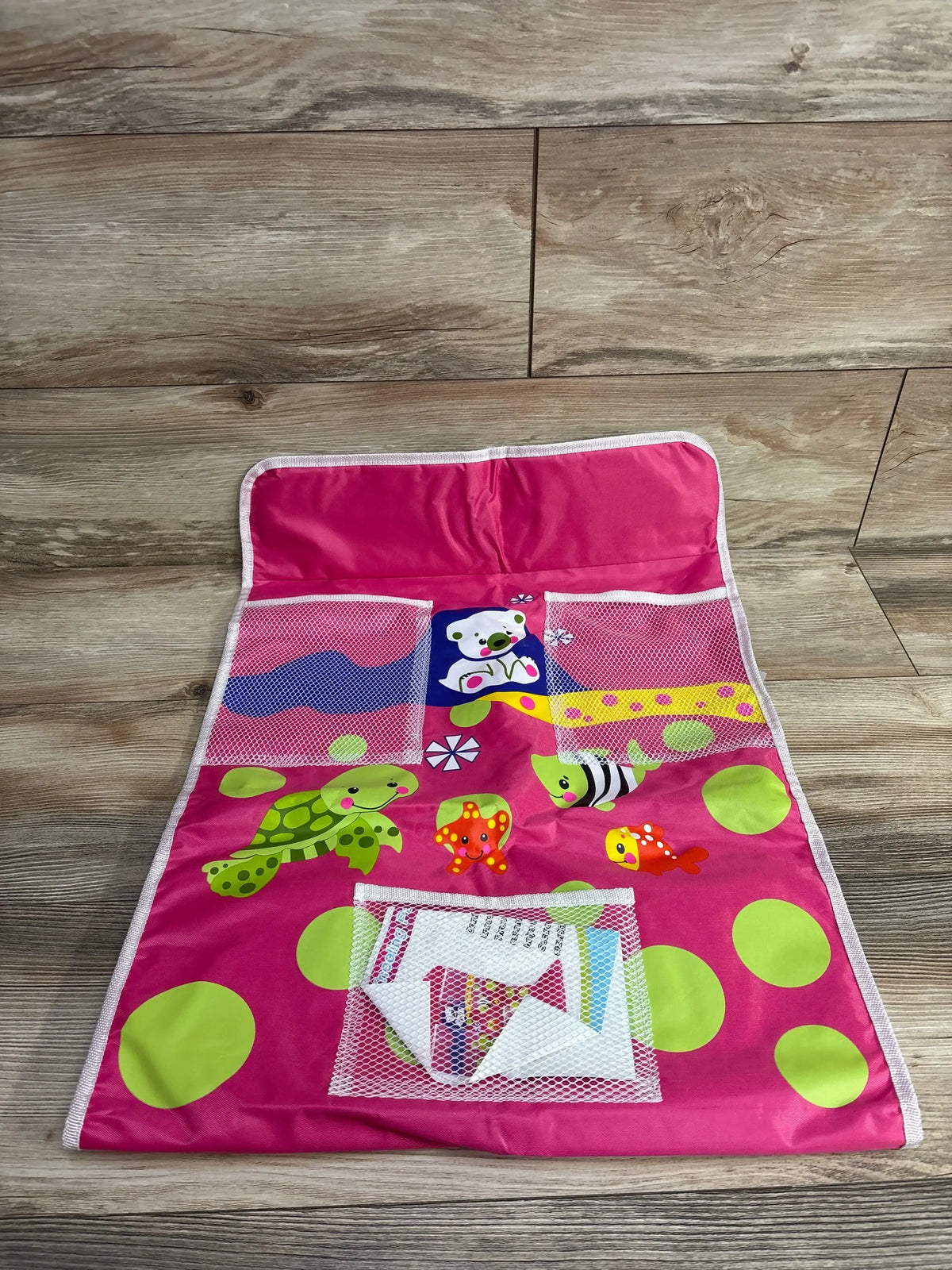 Top-down of pink bath kneeling pad with organizer showing mesh pockets, sea prints and green polka dots on wooden floor