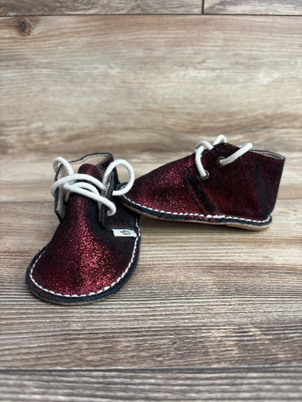 Sparkly red baby shoes with white laces on wooden floor, children's footwear for resale