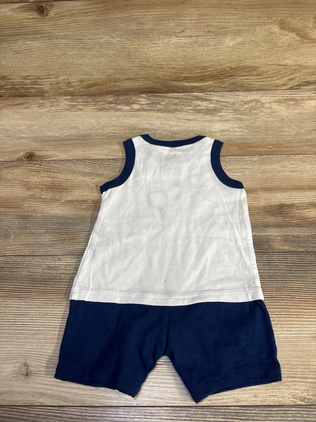 Back view of First Impressions Good Sport shortie romper, white sleeveless top with navy trim and attached navy shorts on wood
